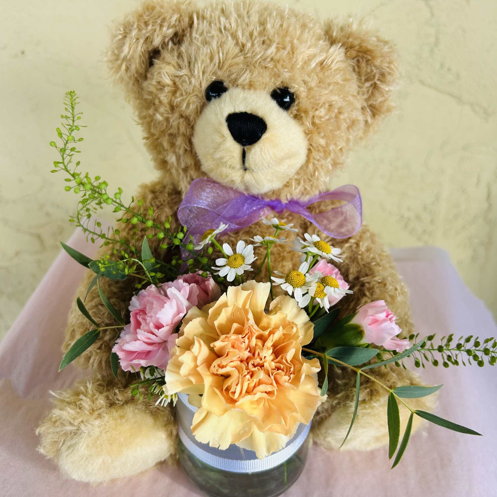 Teddy bear holding a small flower arrangement in a glass vase