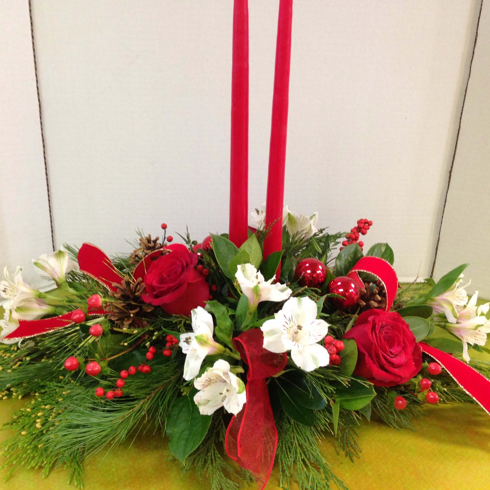 Red roses and white flowers in a low holiday centerpiece with tall red candles