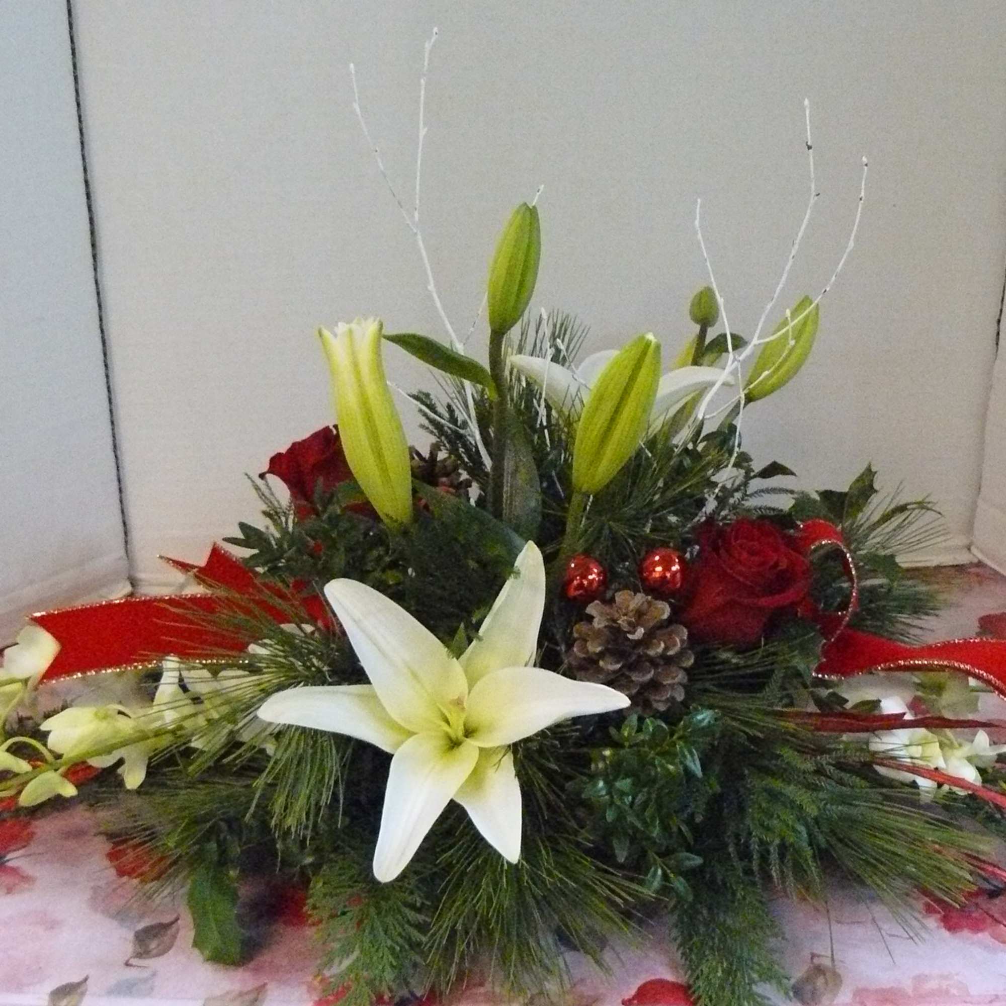 Low floral centerpiece with white lilies, red roses, and red ribbon