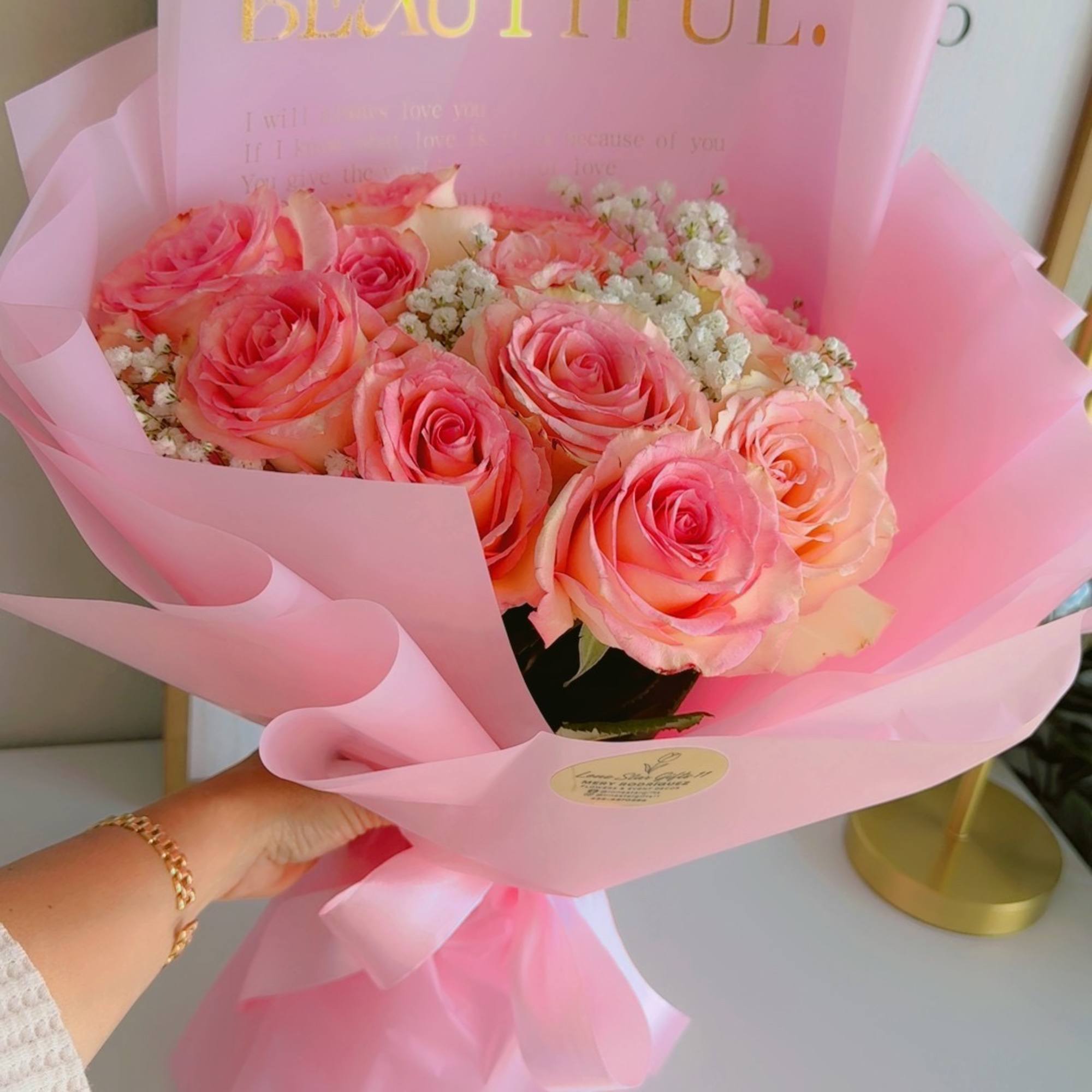 Pink rose bouquet wrapped in translucent pink paper with a gold "BEAUTIFUL" card