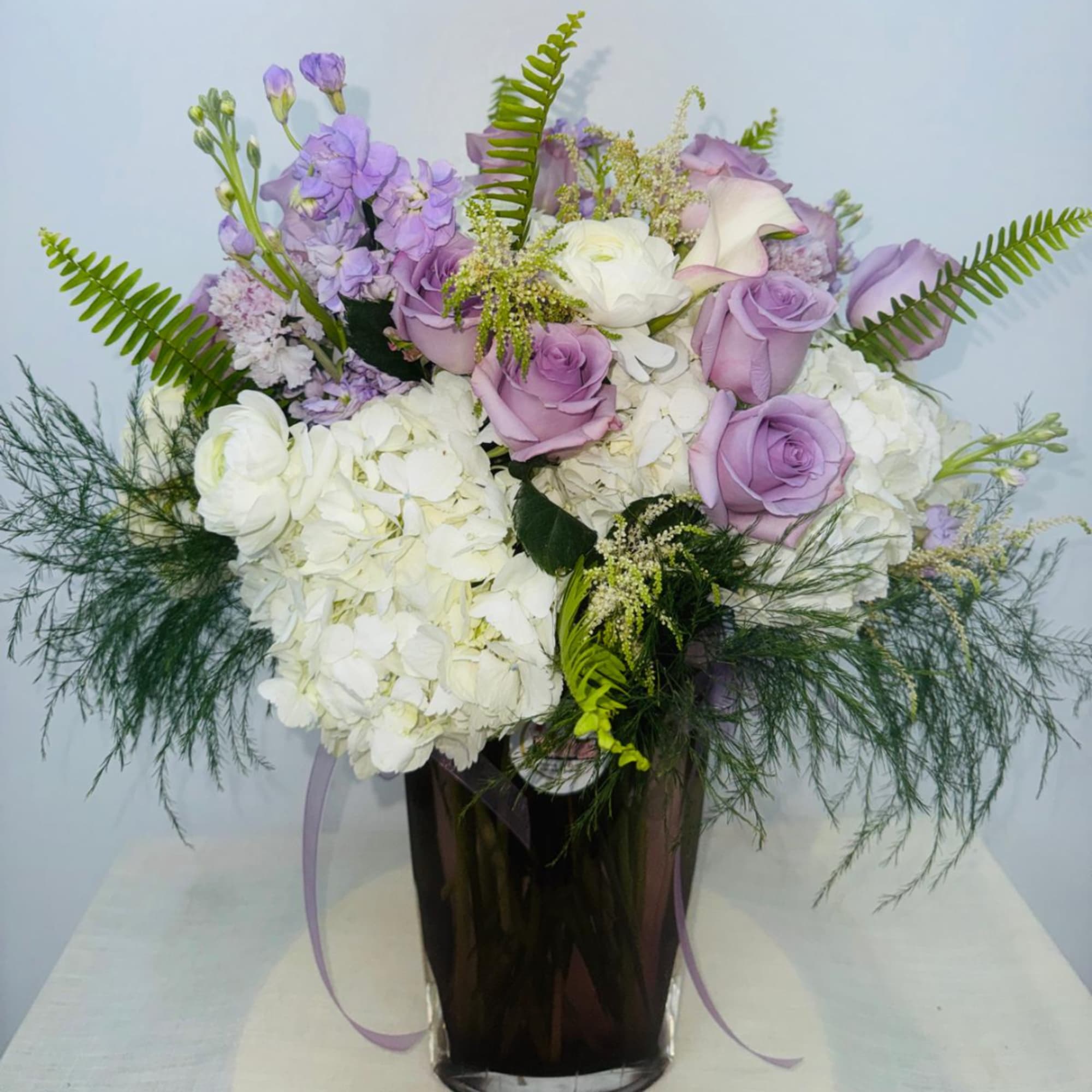 Lavender roses and white hydrangeas in a dark vase with fern accents