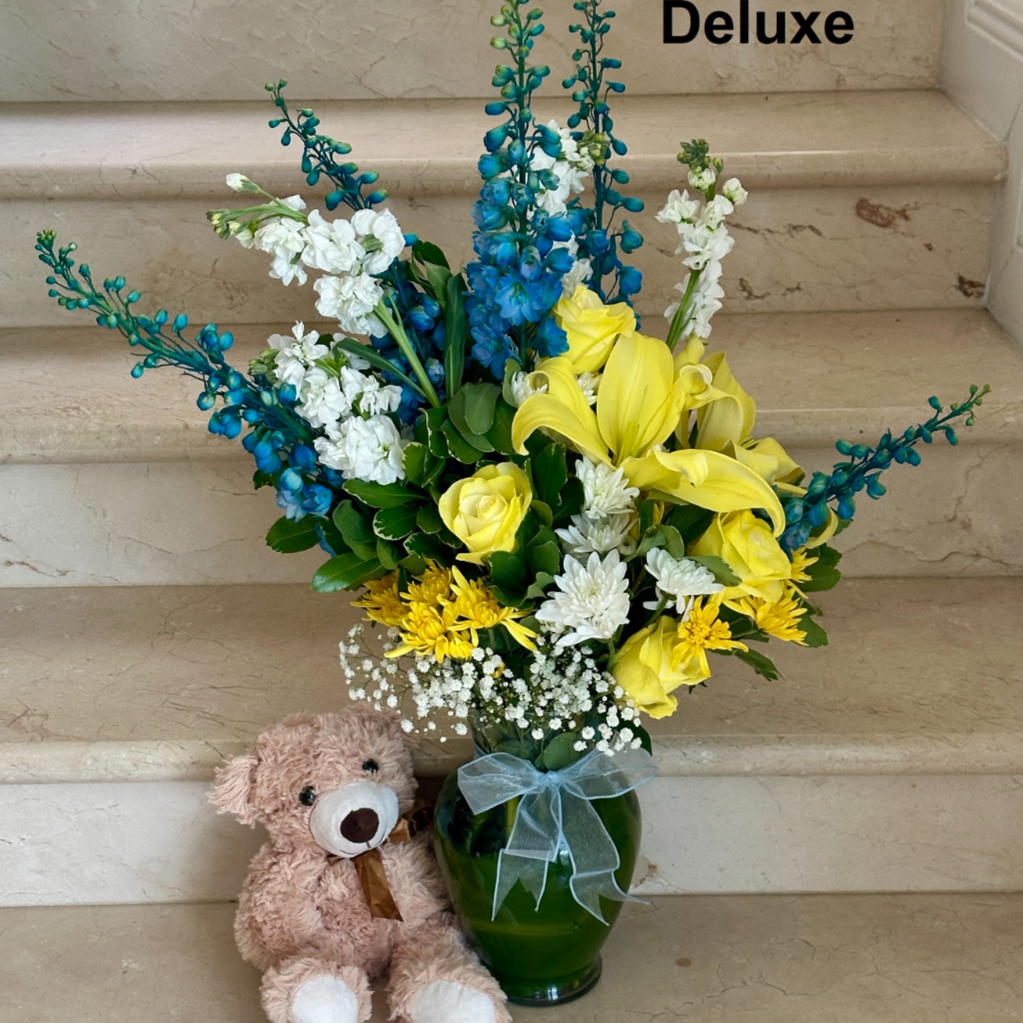 Yellow and white flowers in a green vase with a teddy bear beside it