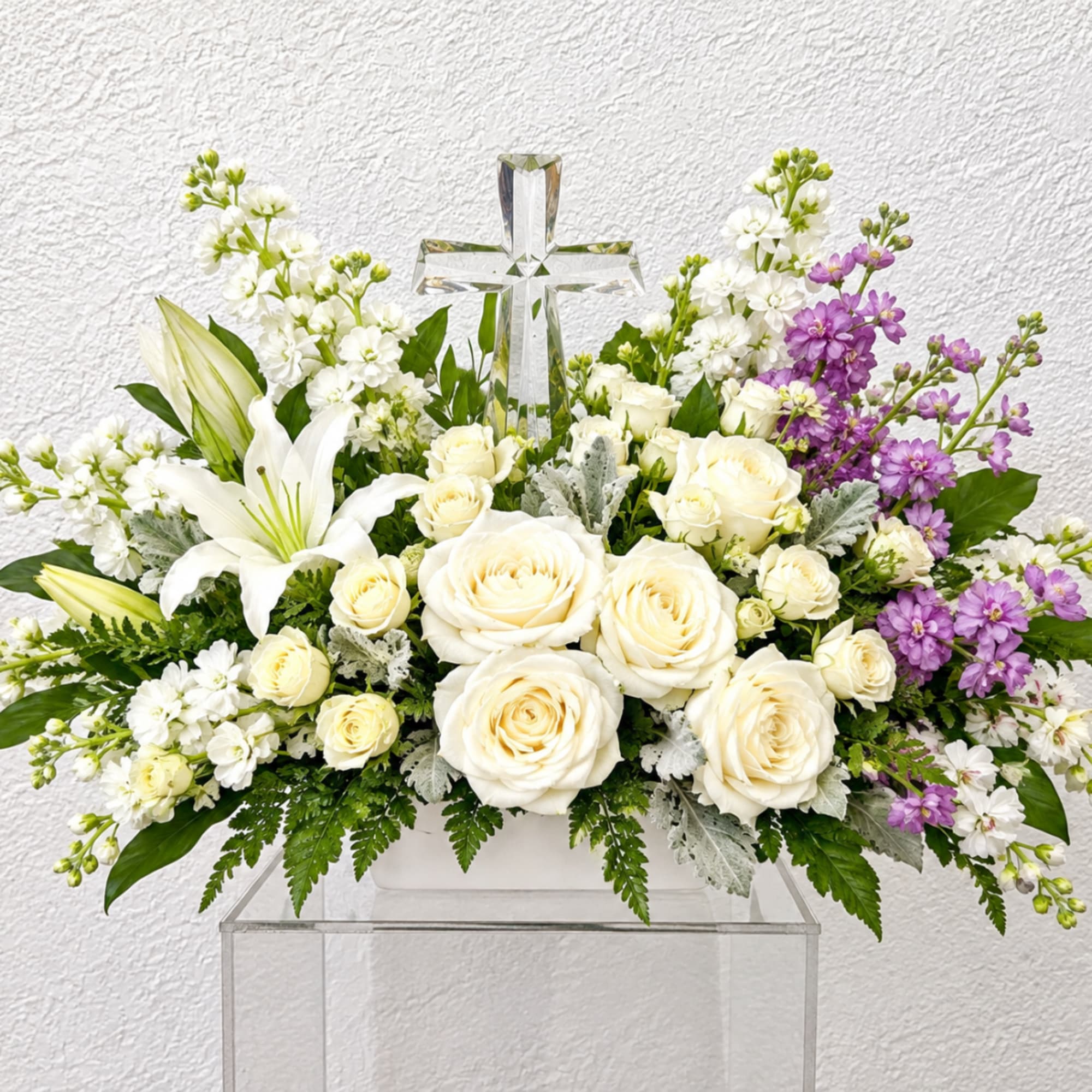 White roses and lilies arranged around a clear cross centerpiece