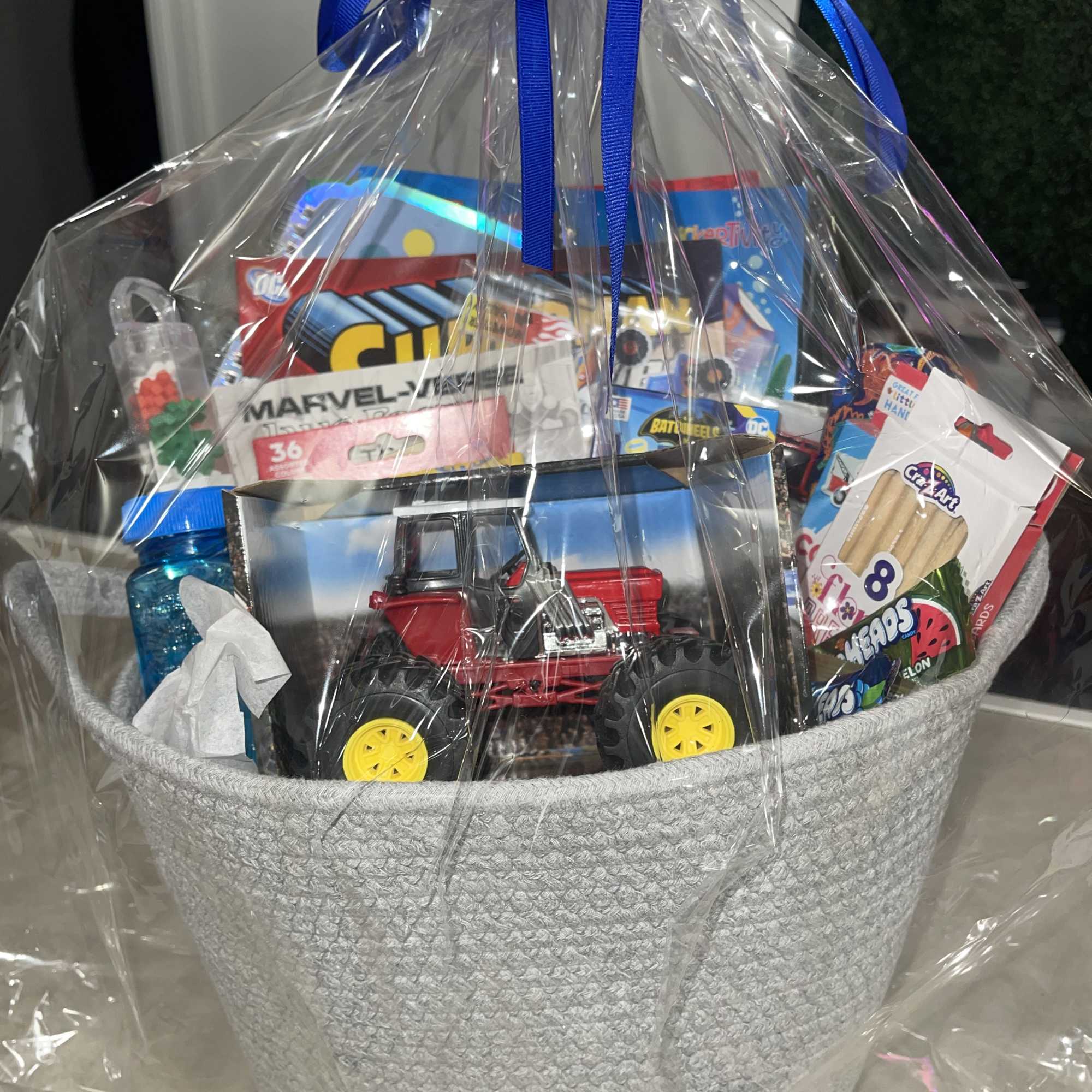 Gift basket with toys and candy wrapped in clear plastic and a blue ribbon