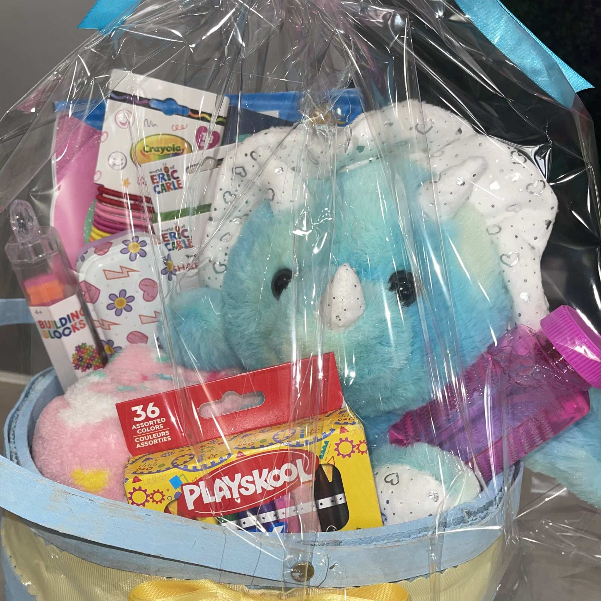 Gift basket with a blue plush unicorn, crayons, and other toys wrapped in cellophane