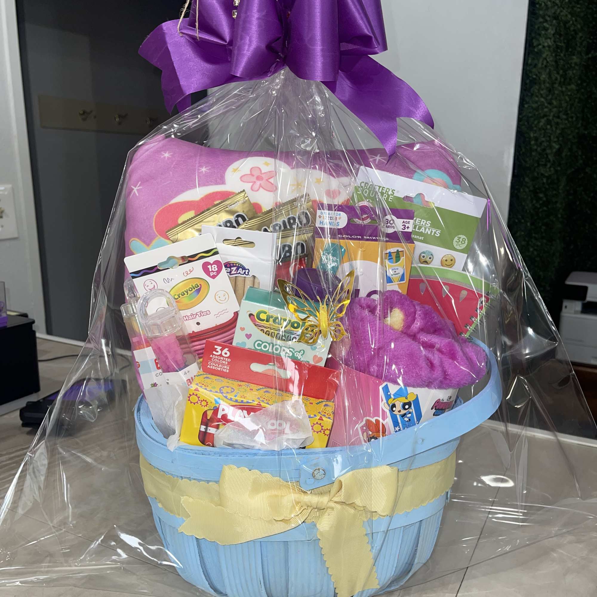 Gift basket with toys and candy wrapped in clear cellophane and a purple bow