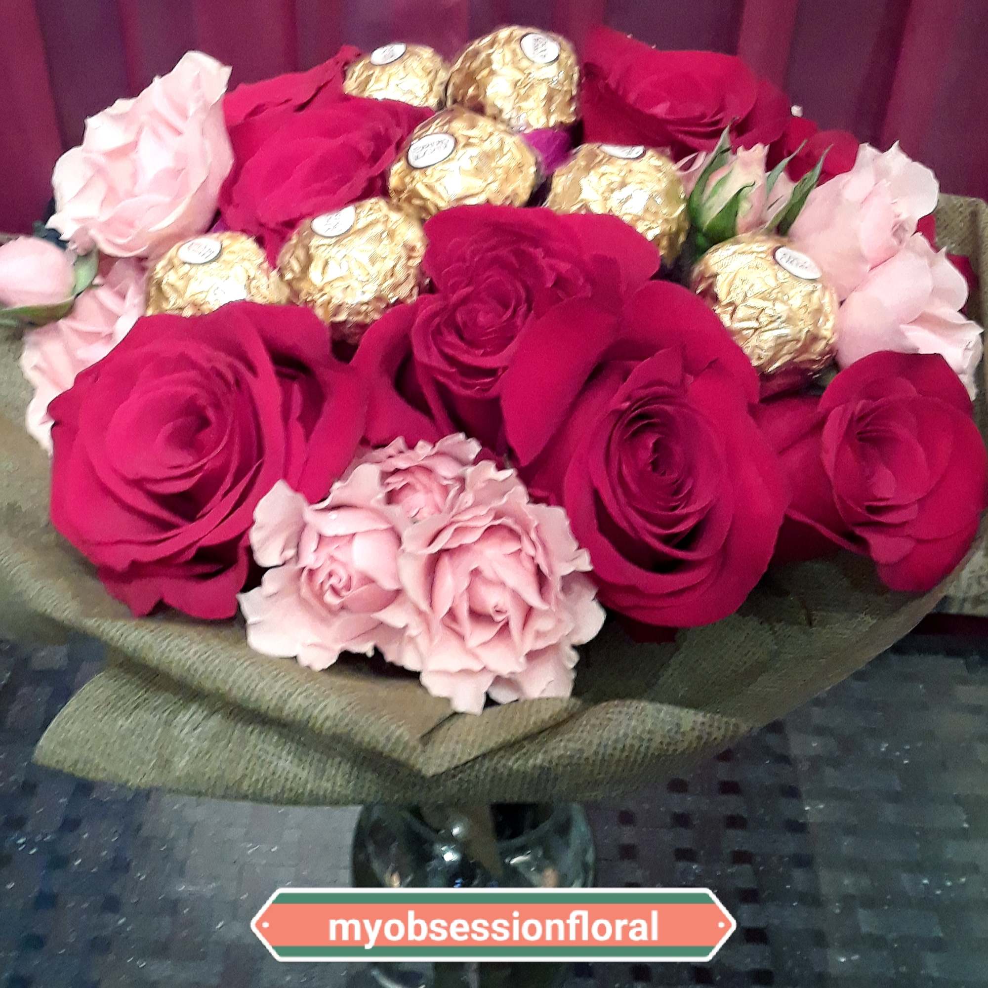 Bouquet of red and pink roses with gold-wrapped chocolates in a glass vase