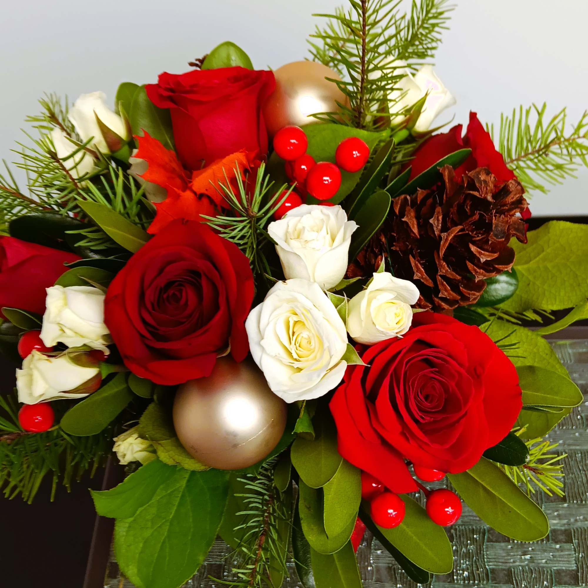 Red and white roses arranged with pinecones and holiday ornaments