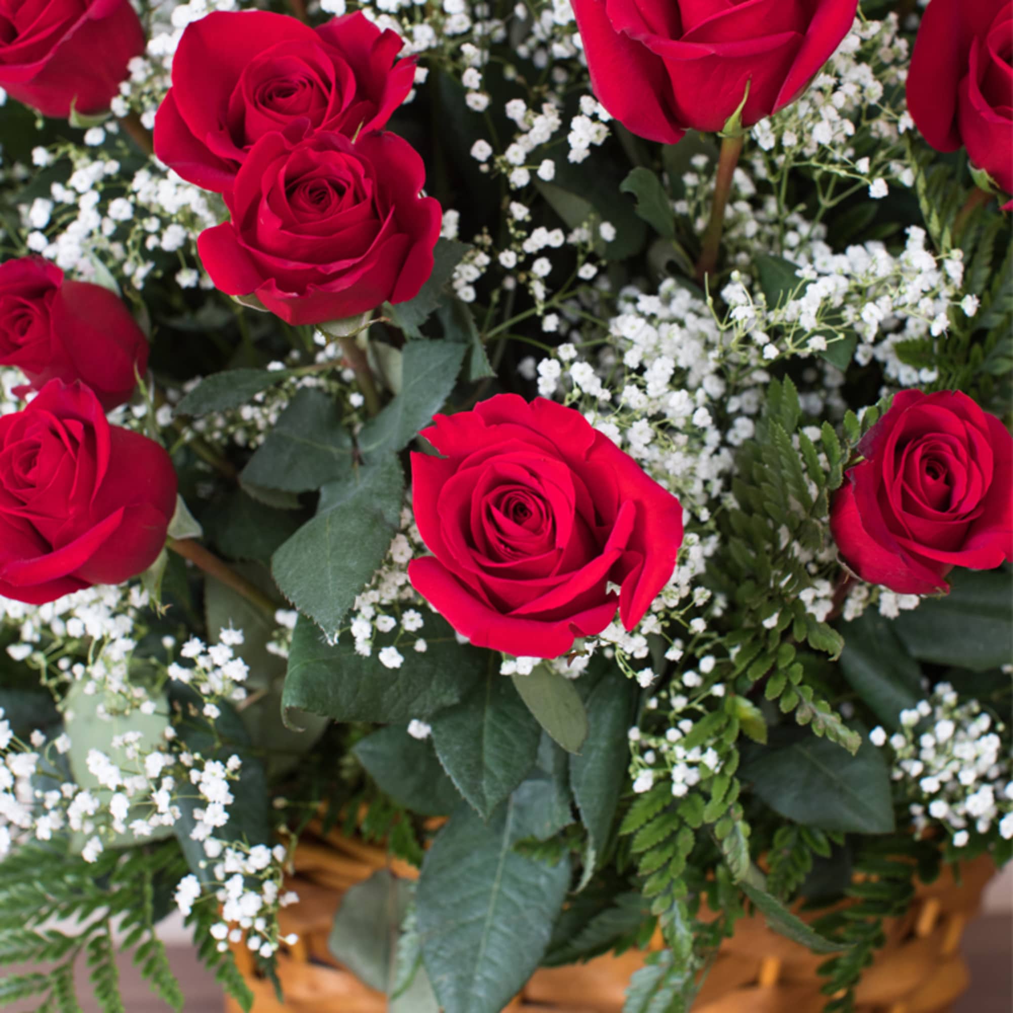 Arrangement of red roses with small white accent flowers in a woven basket