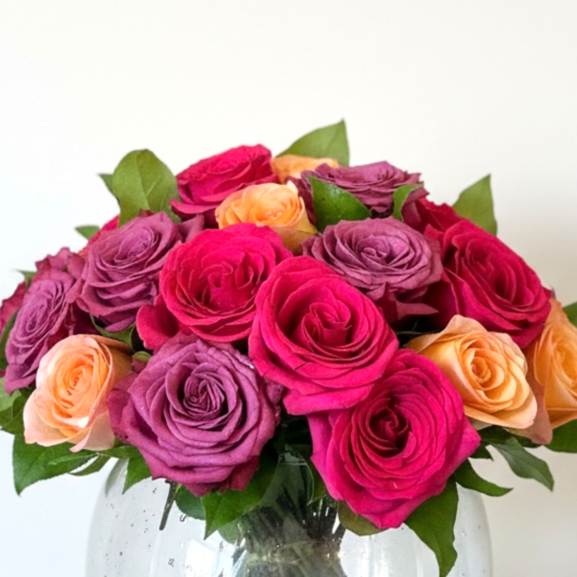 Bouquet of pink, purple, and peach roses in a clear glass vase