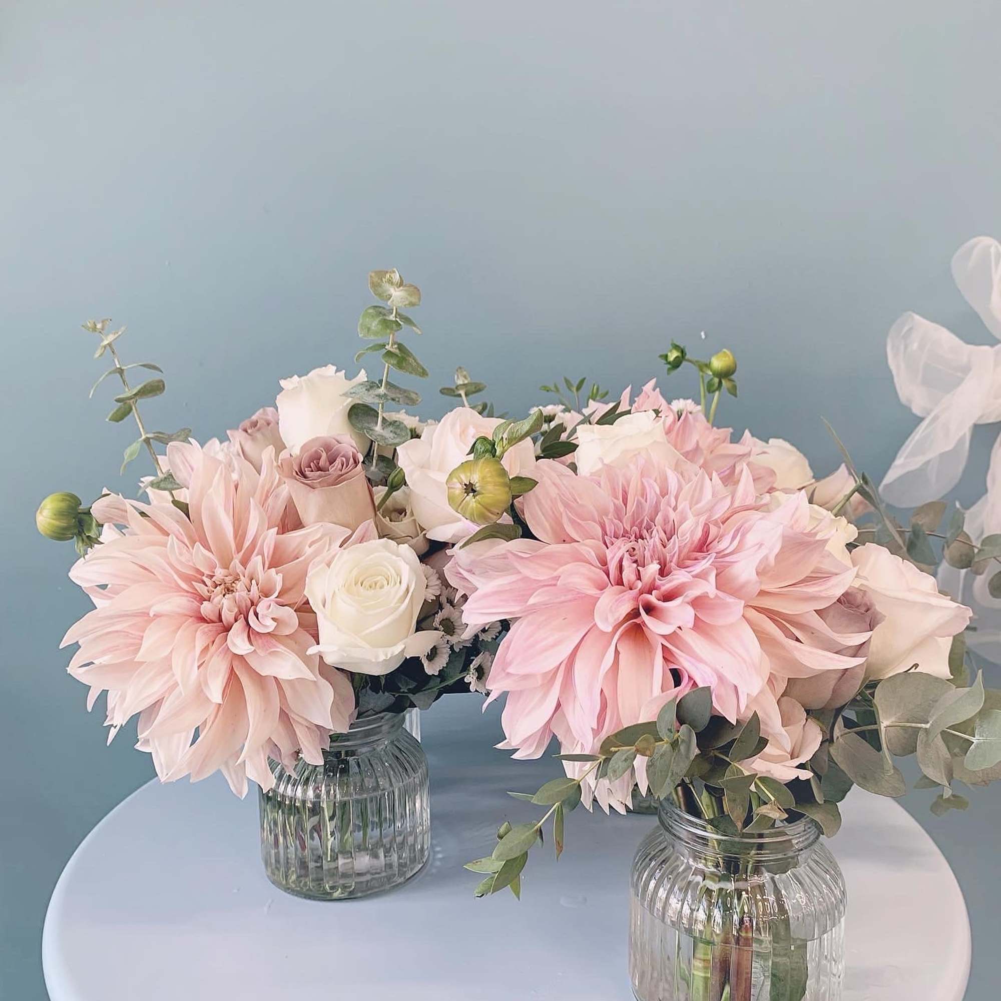Two pastel pink floral arrangements in ribbed glass jars