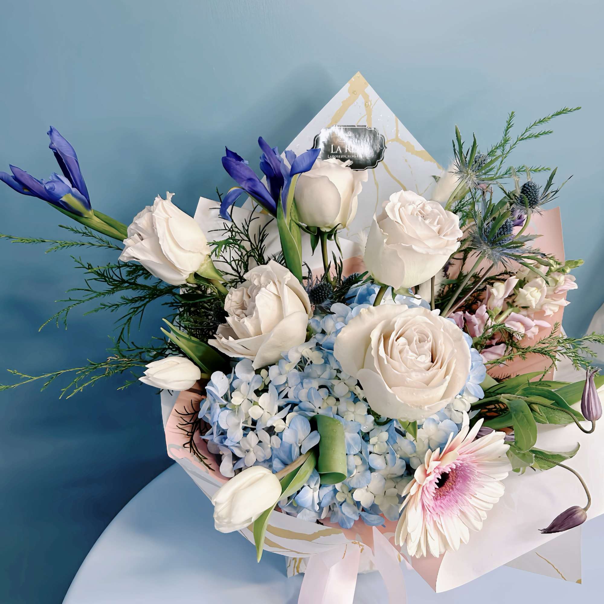 Bouquet of white roses, blue hydrangeas, and purple flowers in pastel wrapping