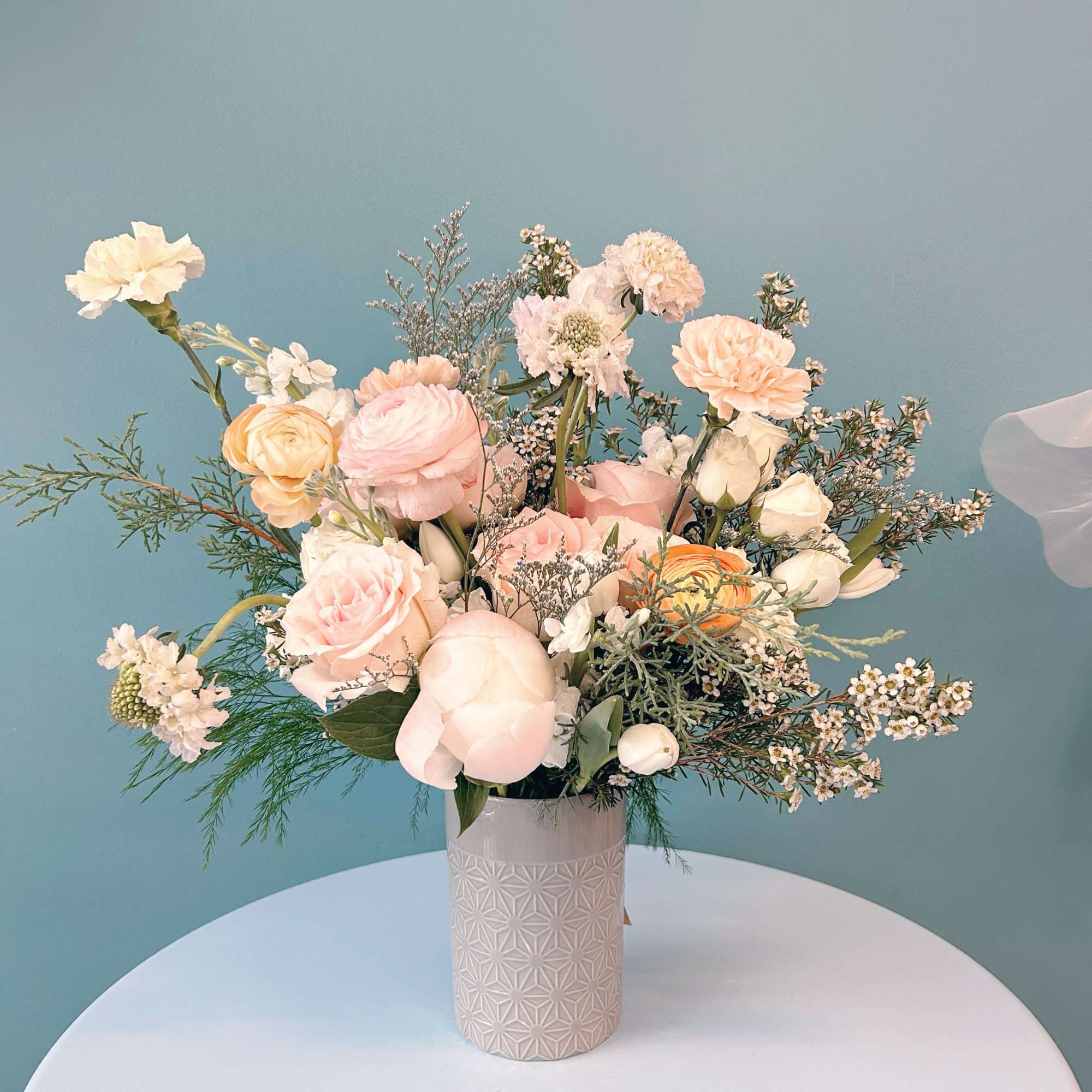 Pastel bouquet of roses, ranunculus, and carnations in a patterned vase