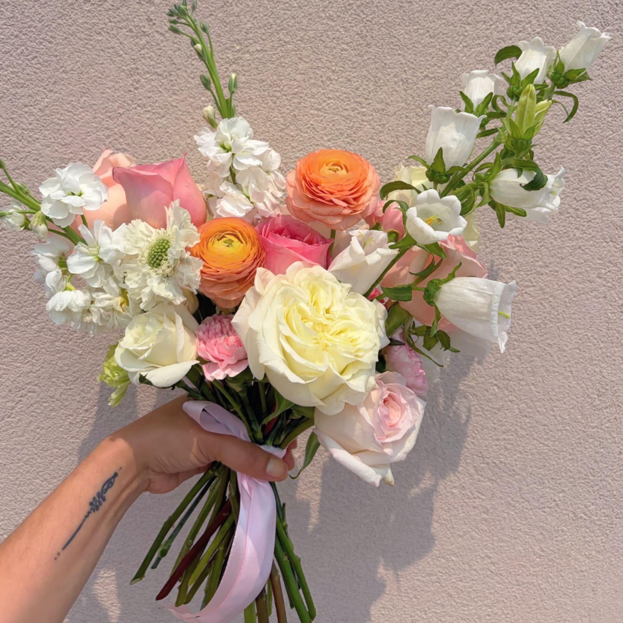 Handheld bouquet of white, pink, and peach flowers tied with a ribbon