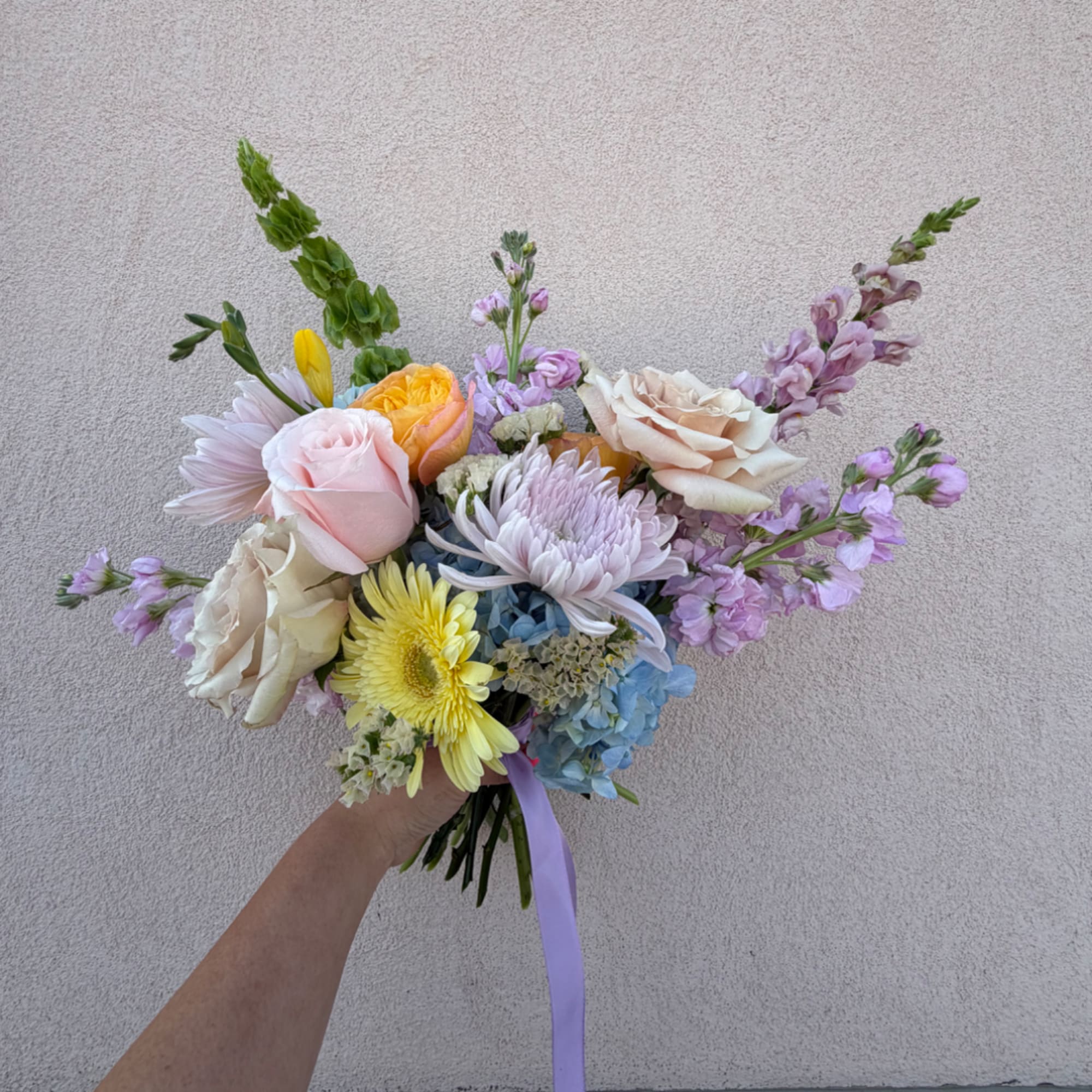 Handheld bouquet of pastel roses, gerbera daisies, and lavender blooms