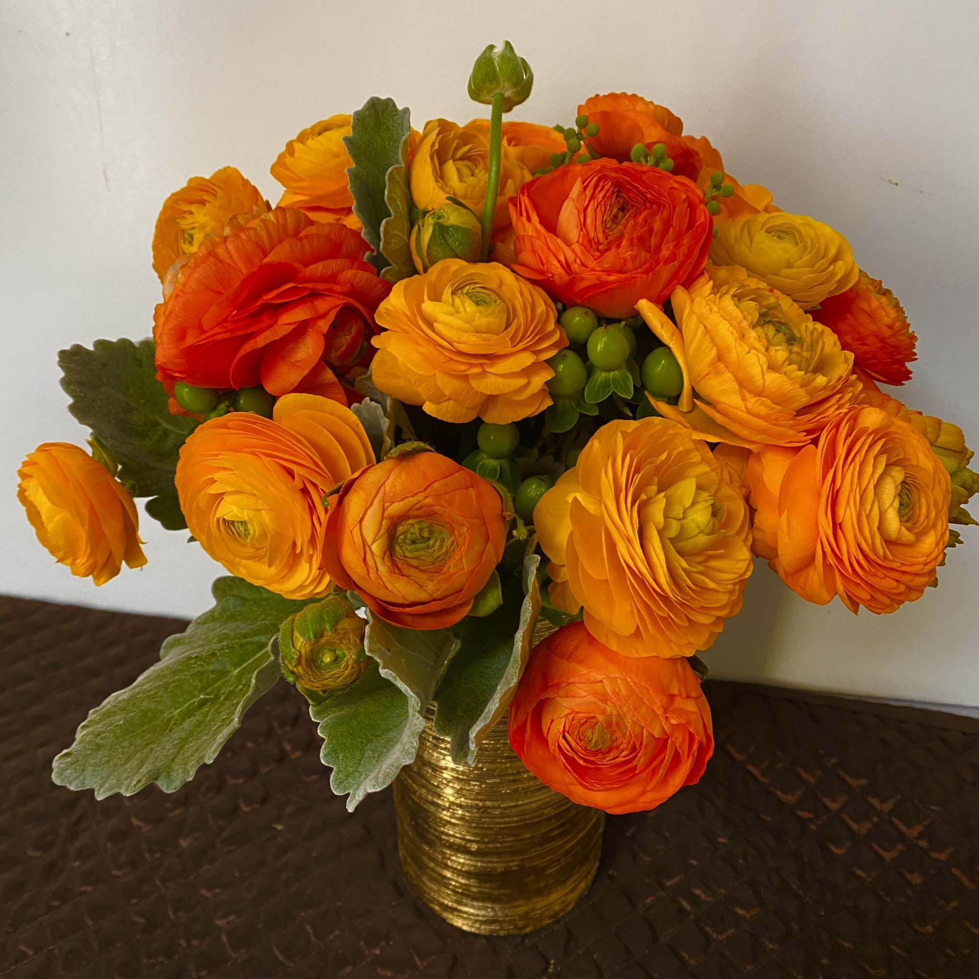 Orange and yellow ranunculus bouquet in a gold vase