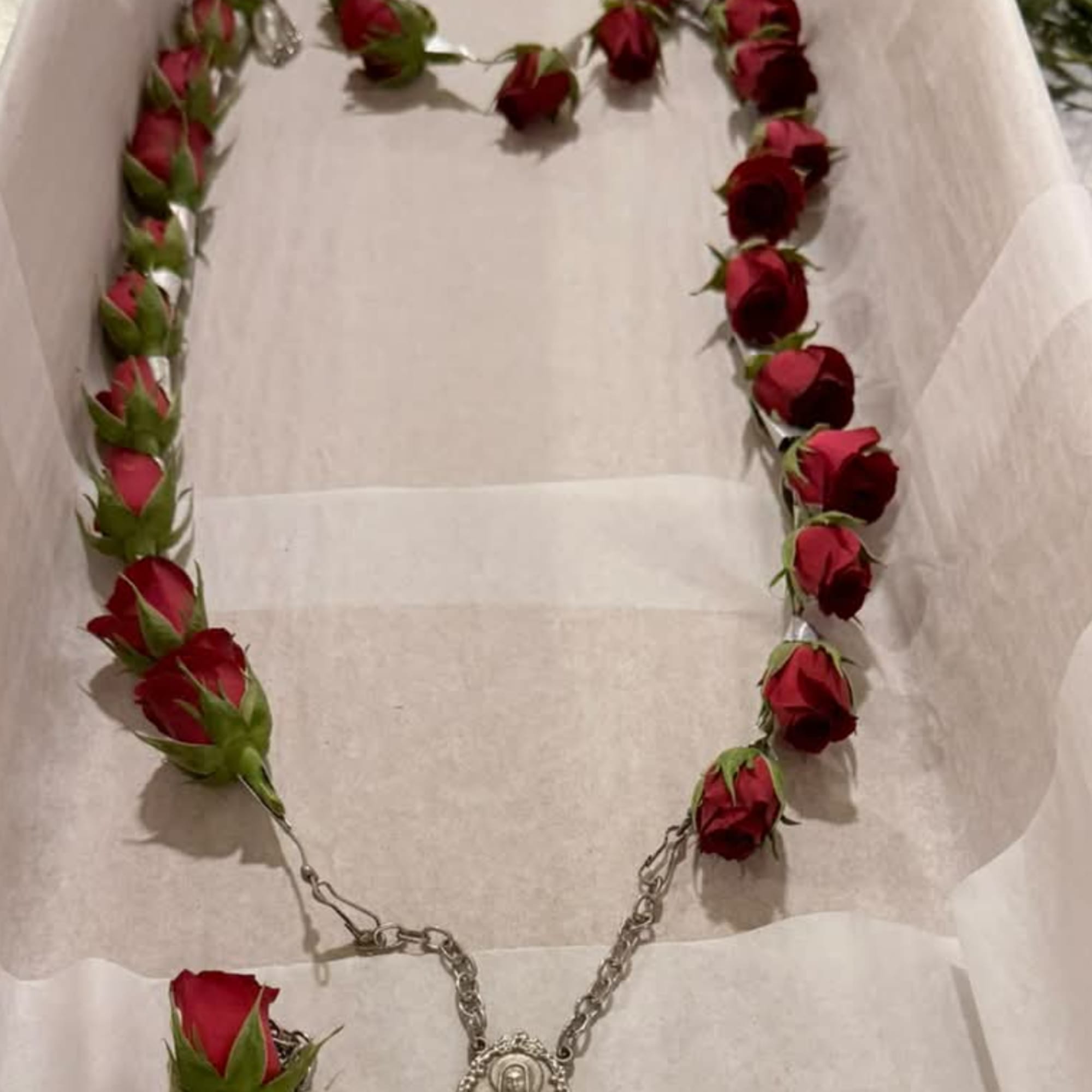 A necklace made of red rosebuds with a silver chain and pendant.