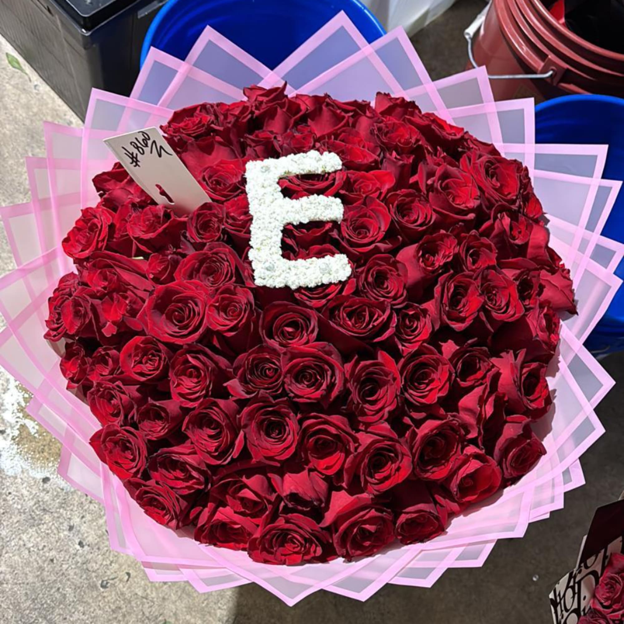 Large bouquet of red roses wrapped in pink paper with a white letter E on top