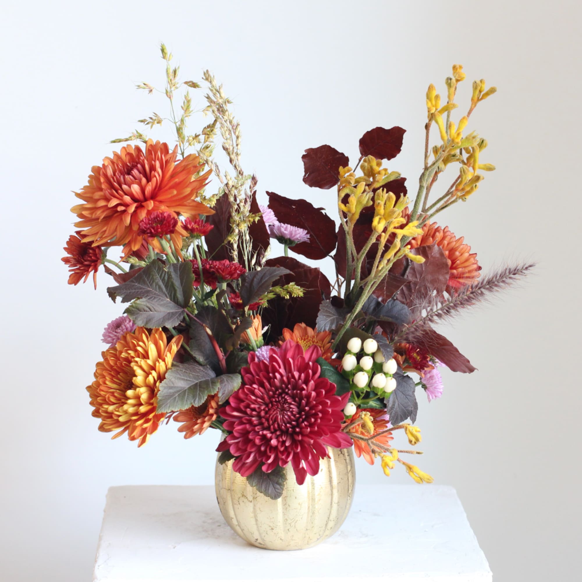Autumn bouquet of orange and burgundy flowers in a gold vase