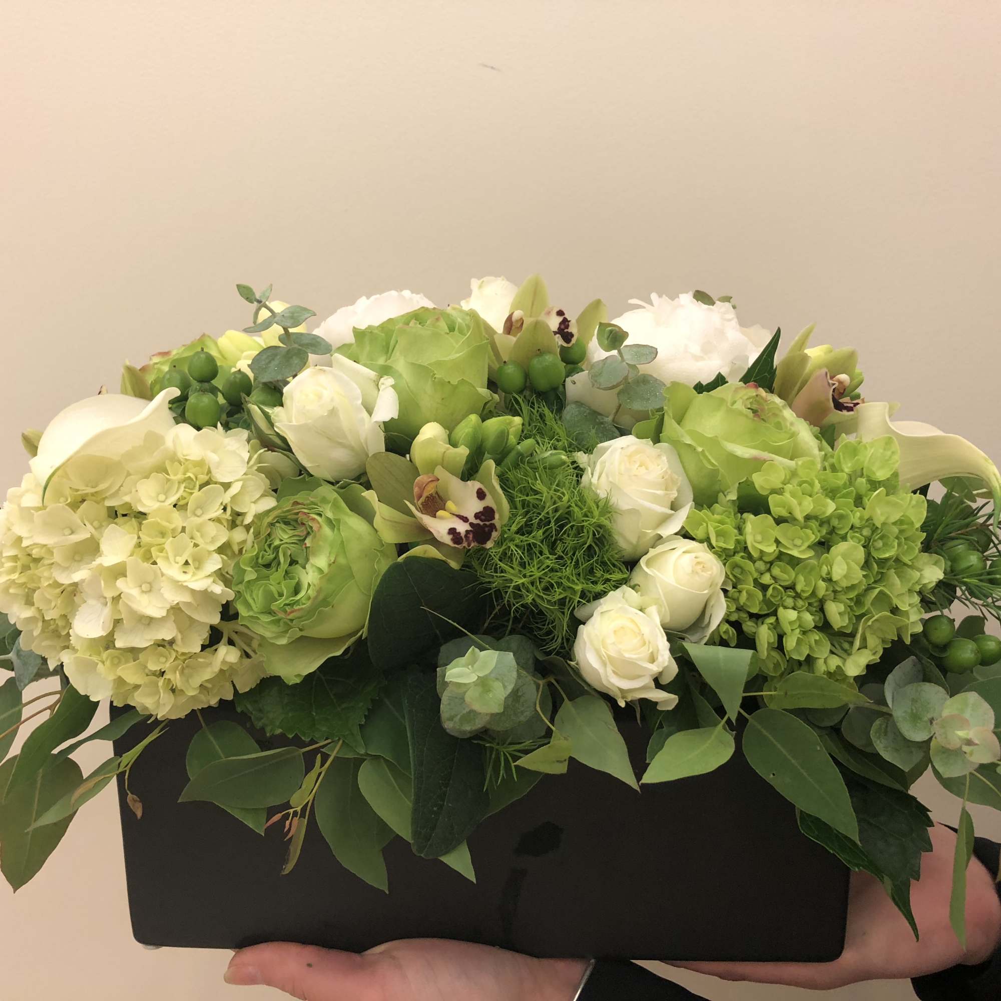 Green and white floral arrangement in a black rectangular container