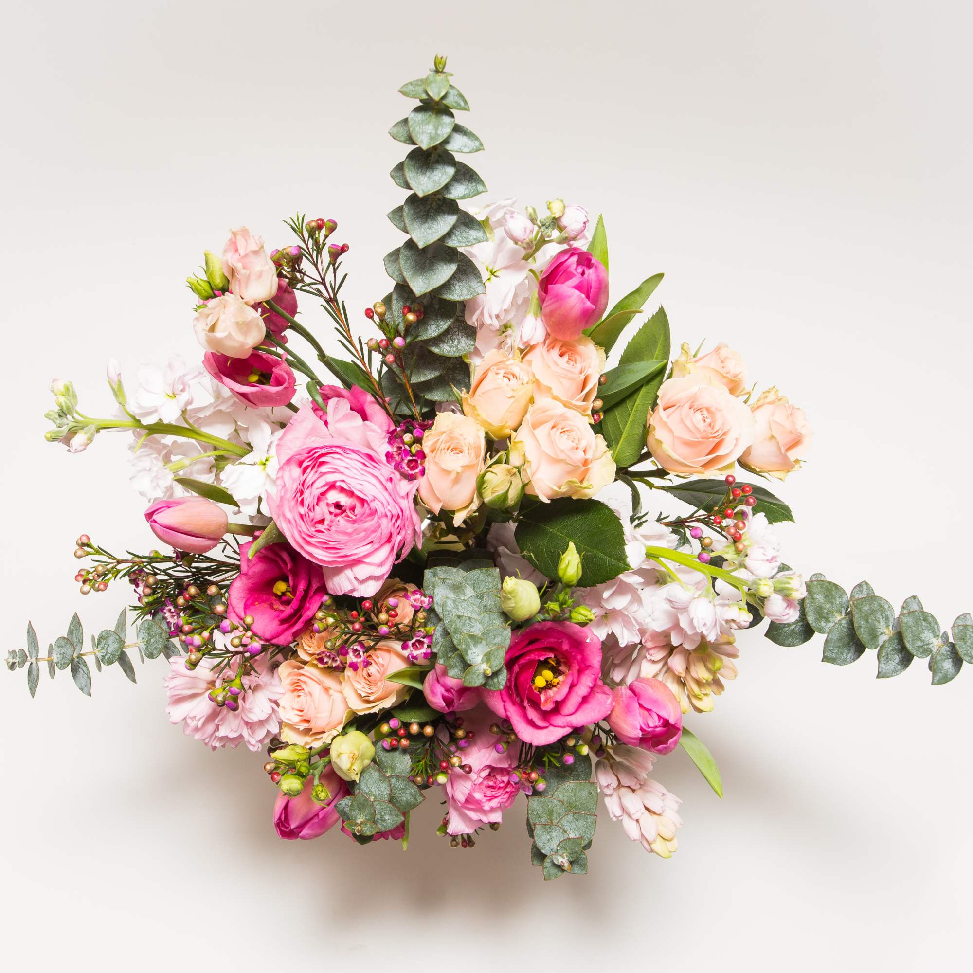 Pink and peach floral arrangement with eucalyptus on a white background