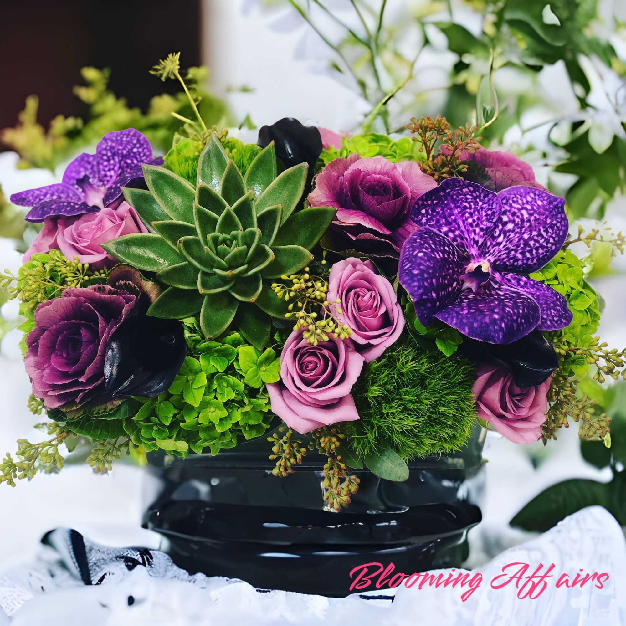 Purple orchids and pink roses arranged with a central succulent in a black vase