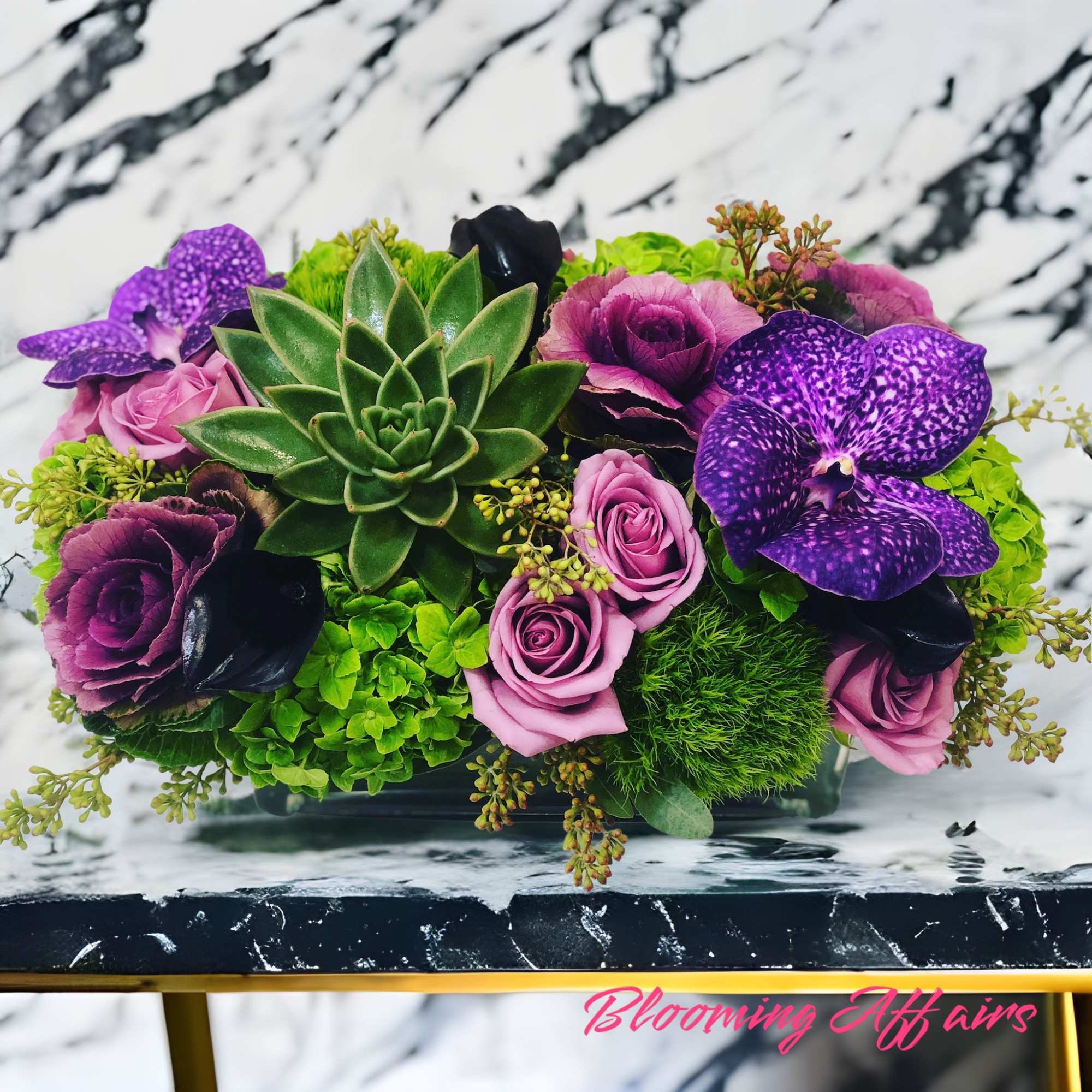 Purple and pink floral arrangement with a central succulent in a rectangular container