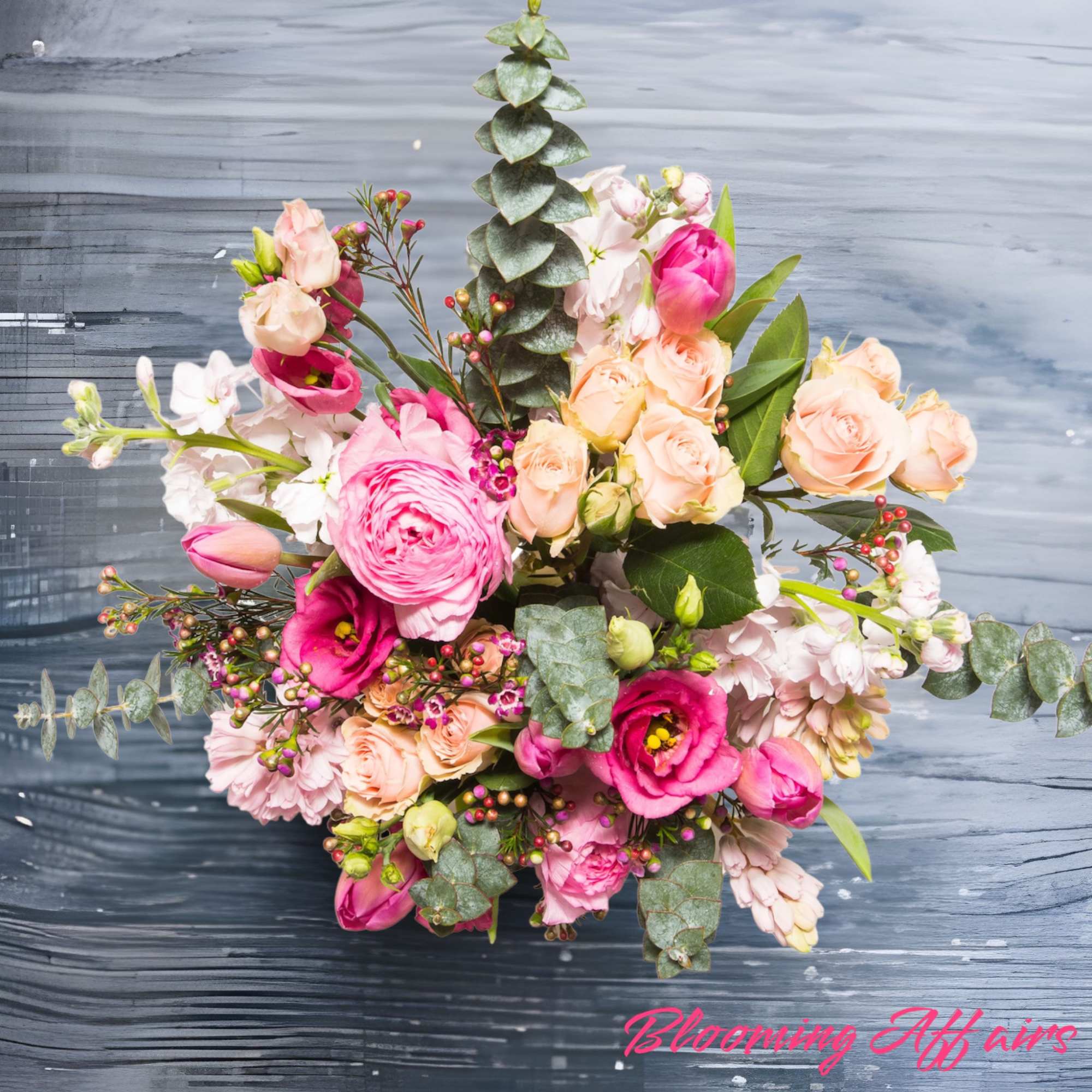 Pink and peach floral bouquet with eucalyptus on a dark wood surface