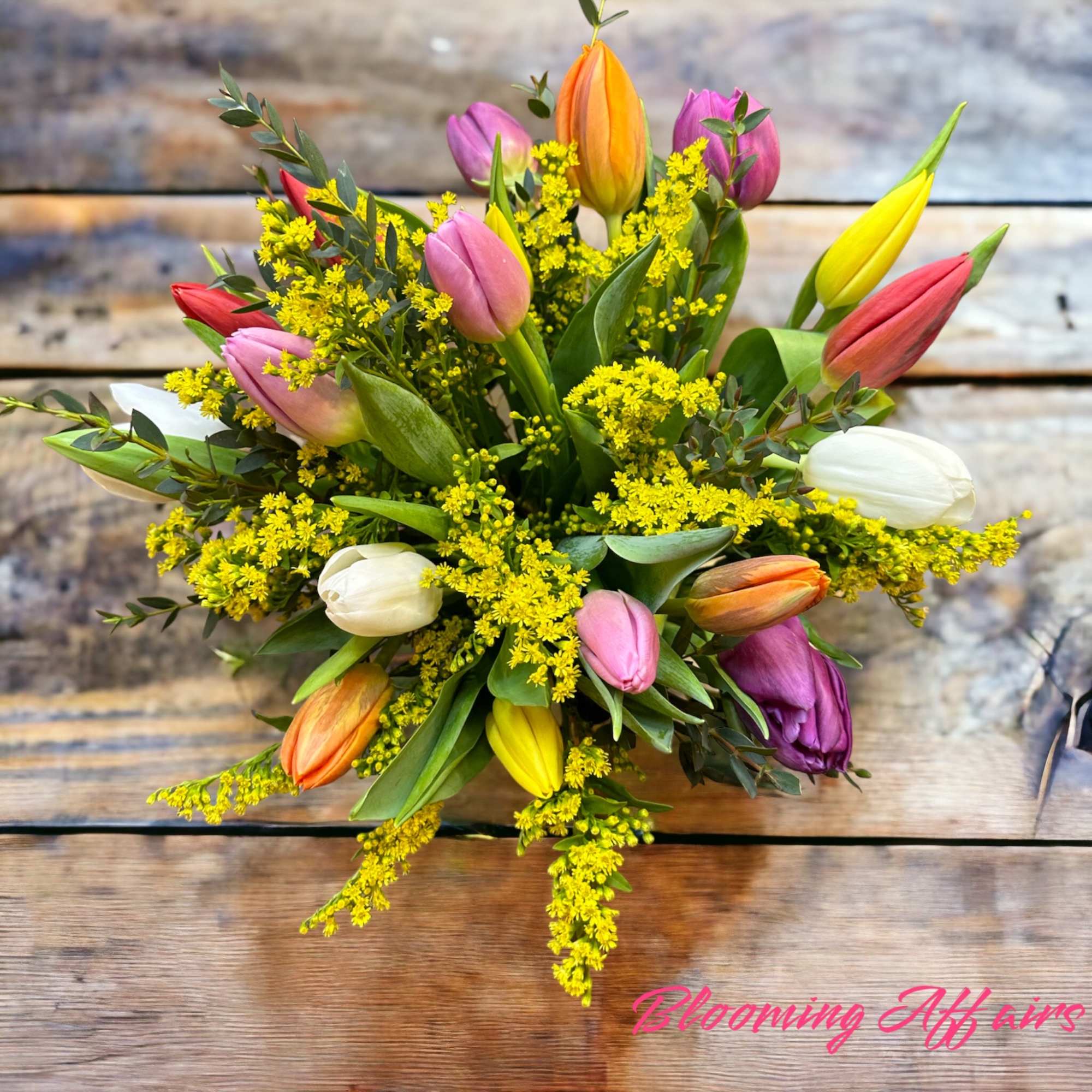 Colorful tulip bouquet with yellow filler flowers on a wooden surface