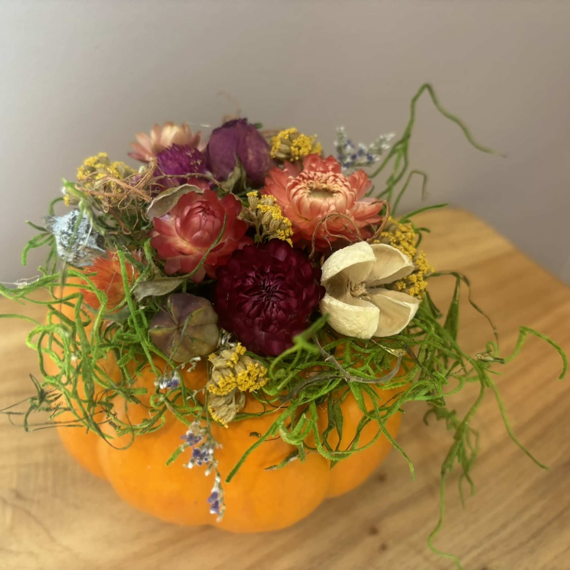 Mixed flowers arranged in a pumpkin-shaped container with curly greenery