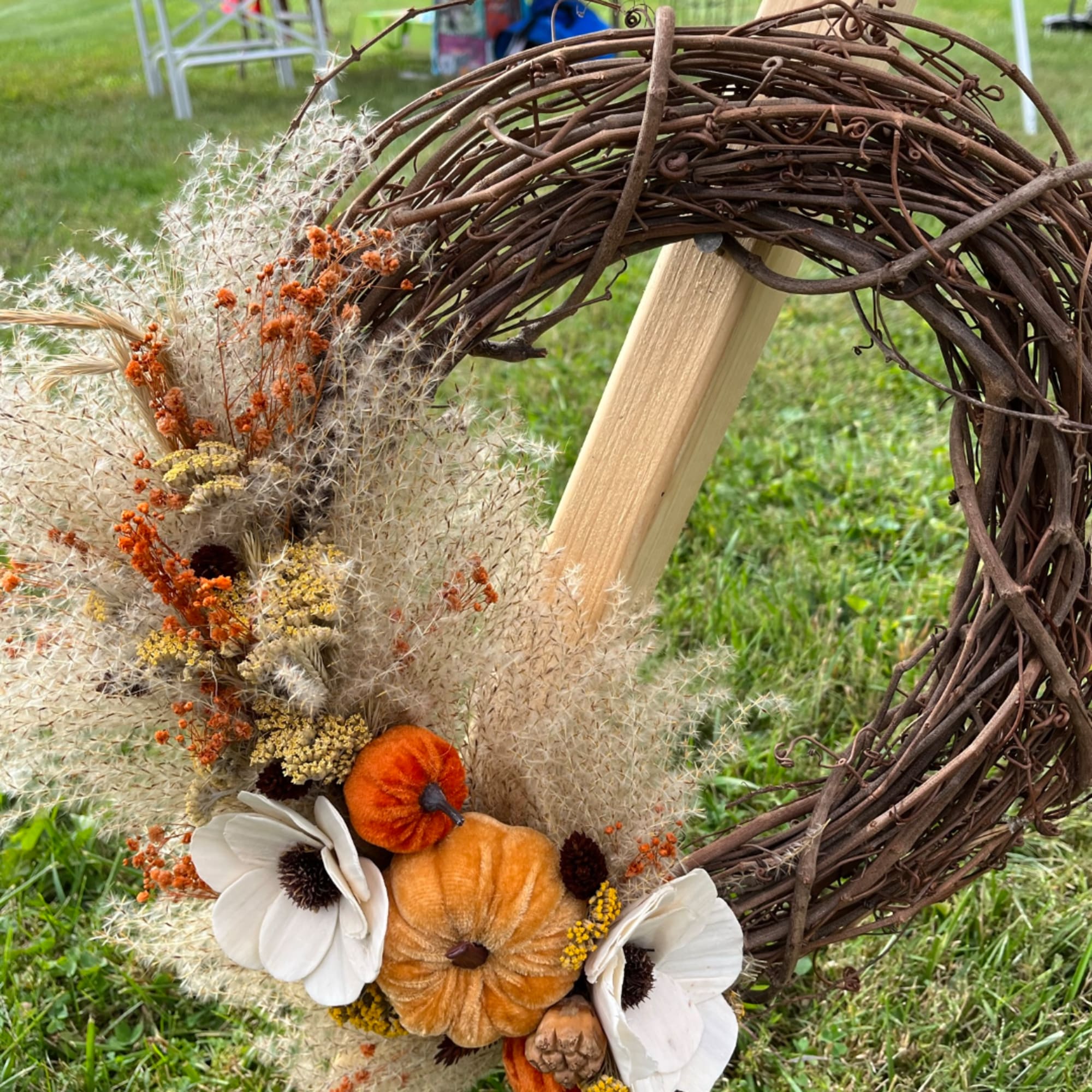 Rustic grapevine wreath with white flowers and orange pumpkins on a grassy lawn