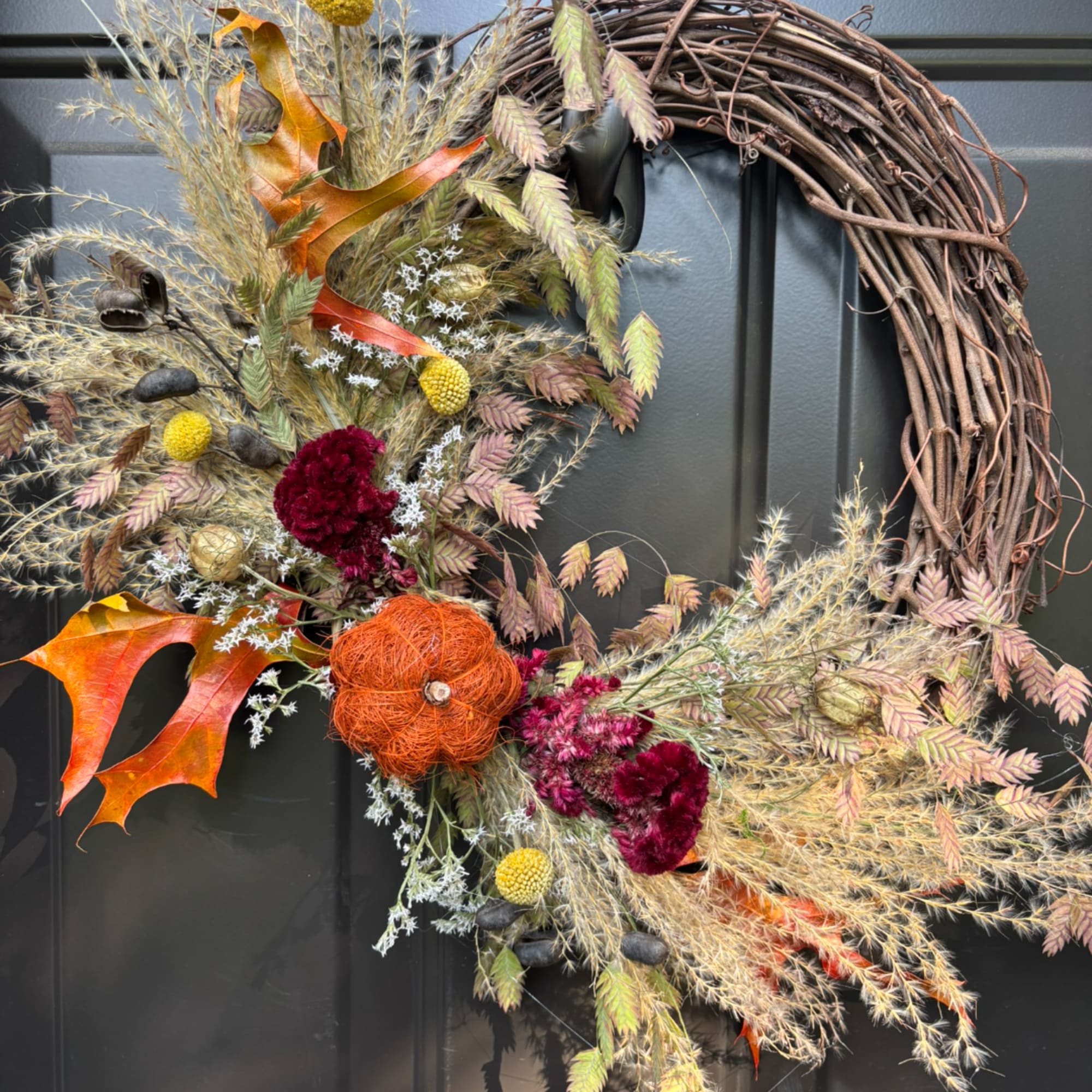 Autumn wreath with dried flowers and orange pumpkin accents on a dark door