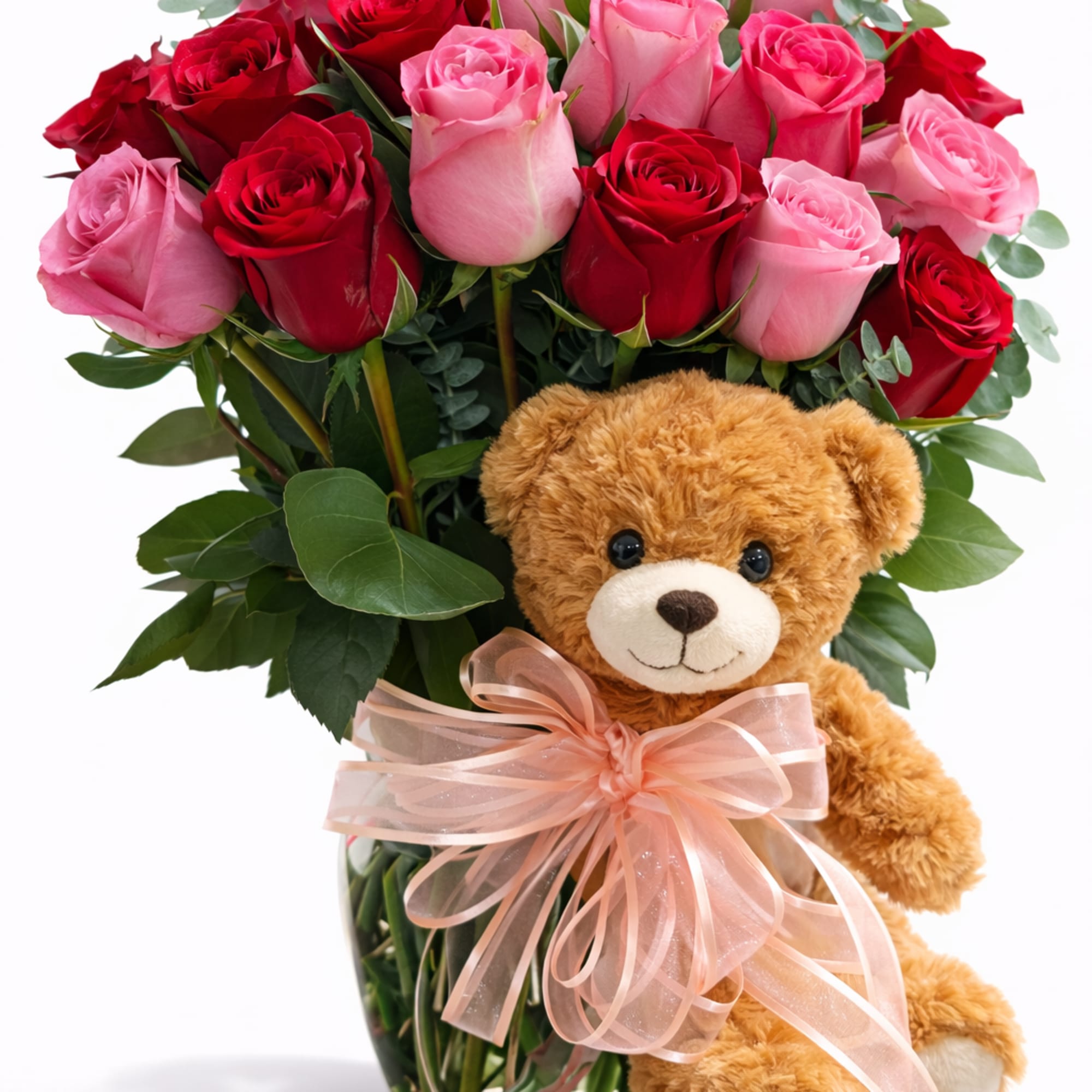 Pink and red roses in a glass vase with a teddy bear and ribbon