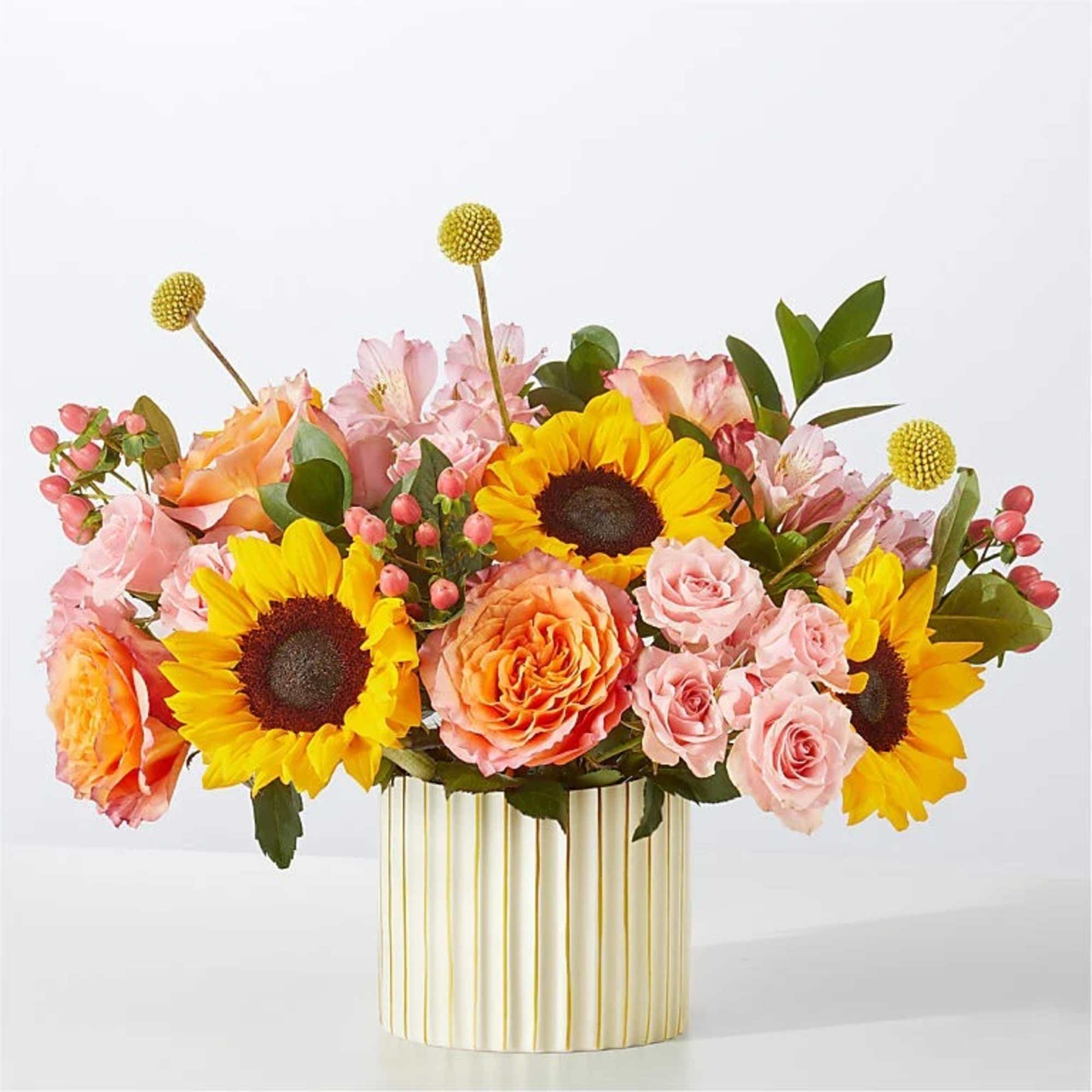 Mixed bouquet of sunflowers, roses, and pink blooms in a striped vase