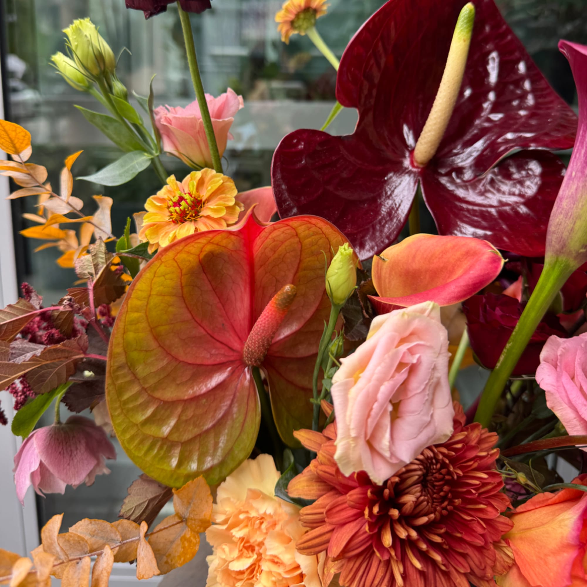 Mixed bouquet with burgundy anthuriums, pink roses, and orange blooms