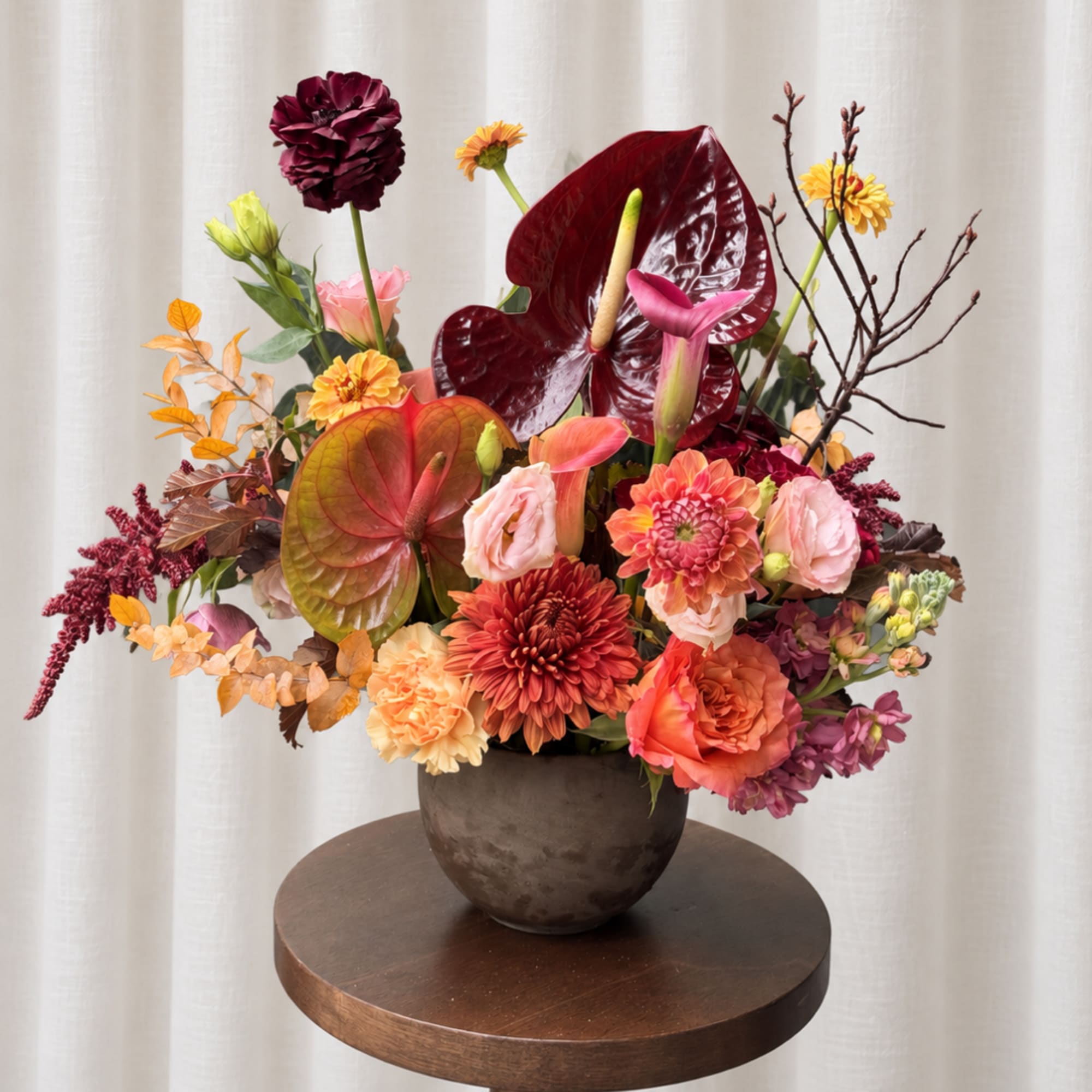 Colorful floral arrangement in a dark vase with anthuriums and mixed blooms