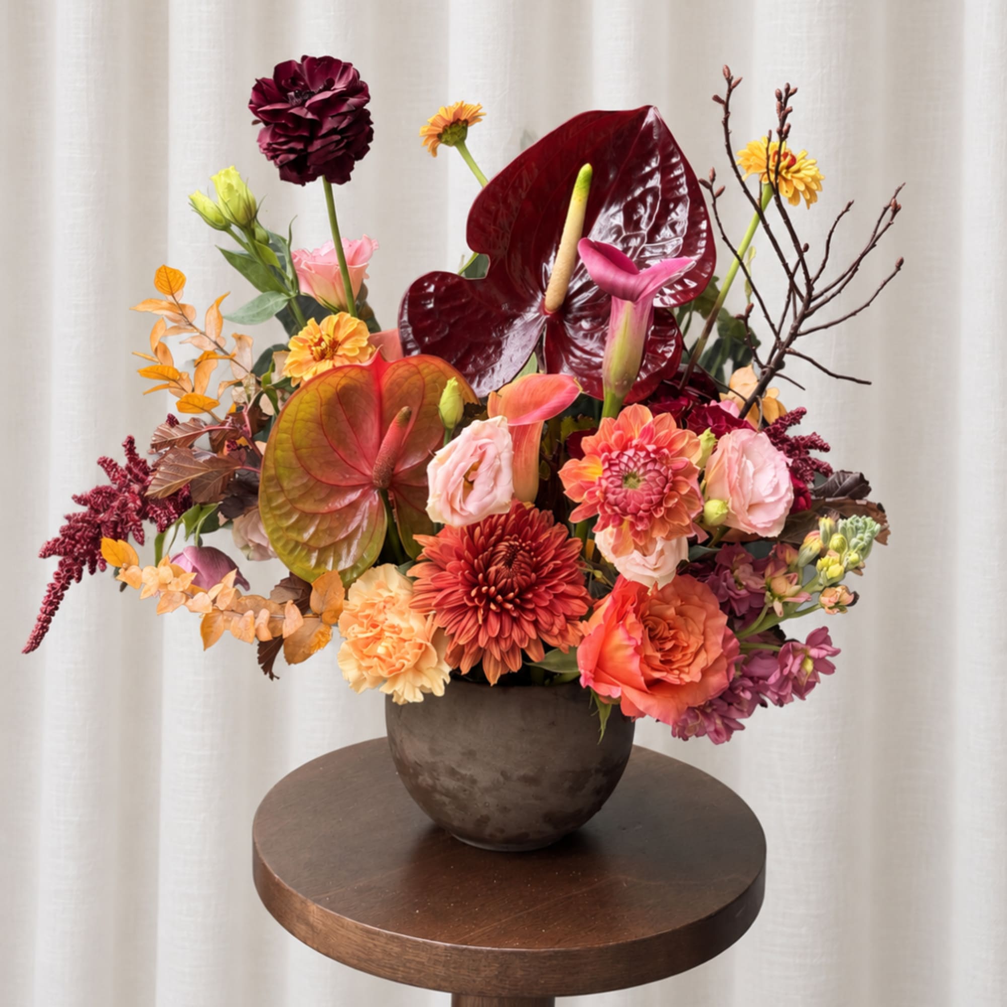 Mixed floral arrangement in a dark vase with burgundy anthuriums and dahlias