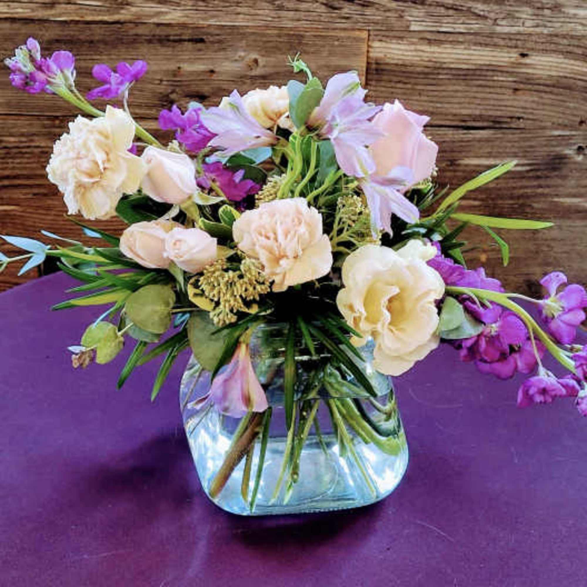 Pastel flower arrangement in a clear glass vase on a purple surface