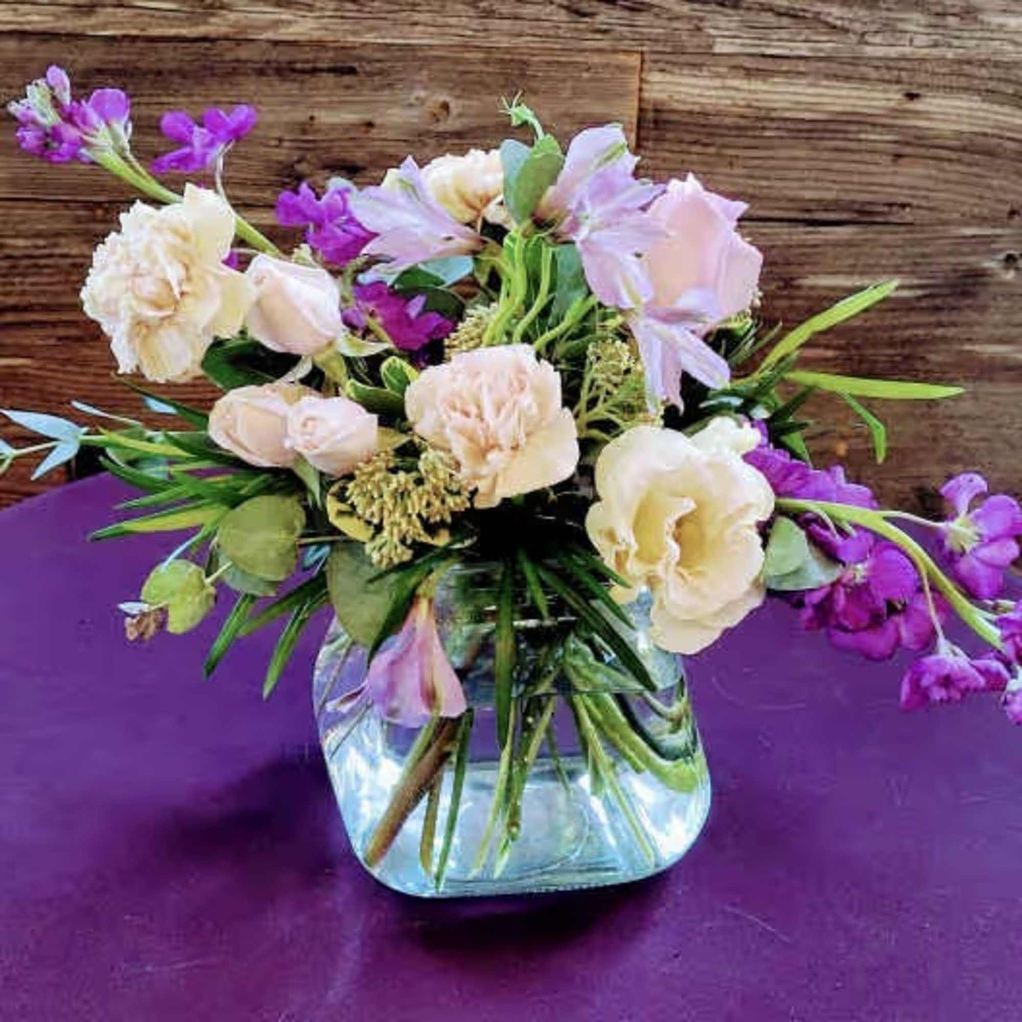Mixed pastel bouquet in a clear glass vase on a purple surface