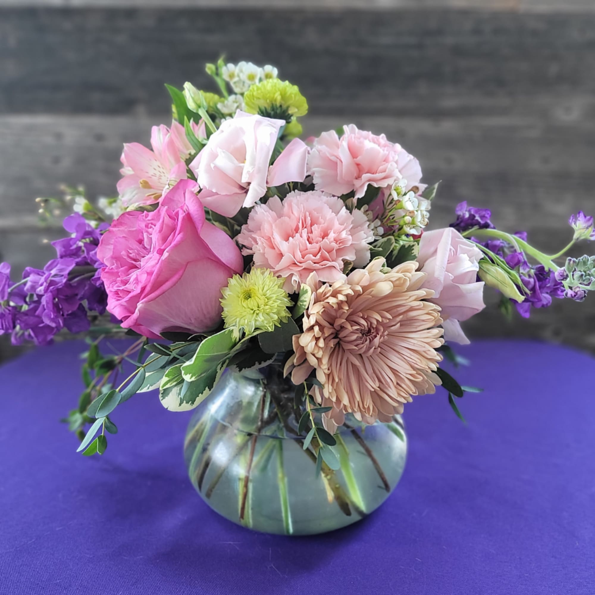 Pink and purple mixed flower arrangement in a round glass vase