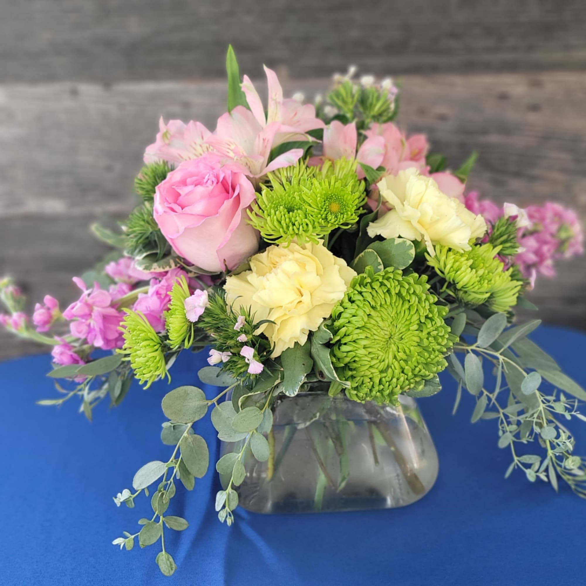 Pink and yellow flowers arranged in a glass vase with trailing greenery