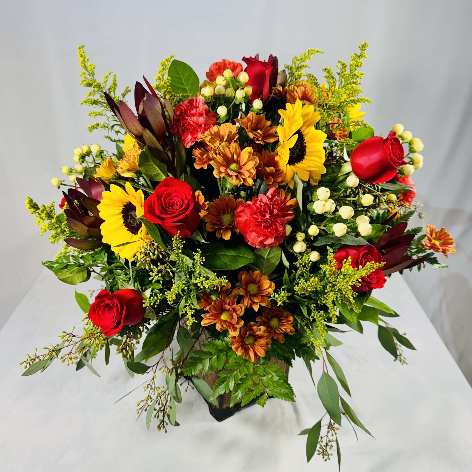Mixed bouquet with red roses, sunflowers, and orange mums in a vase