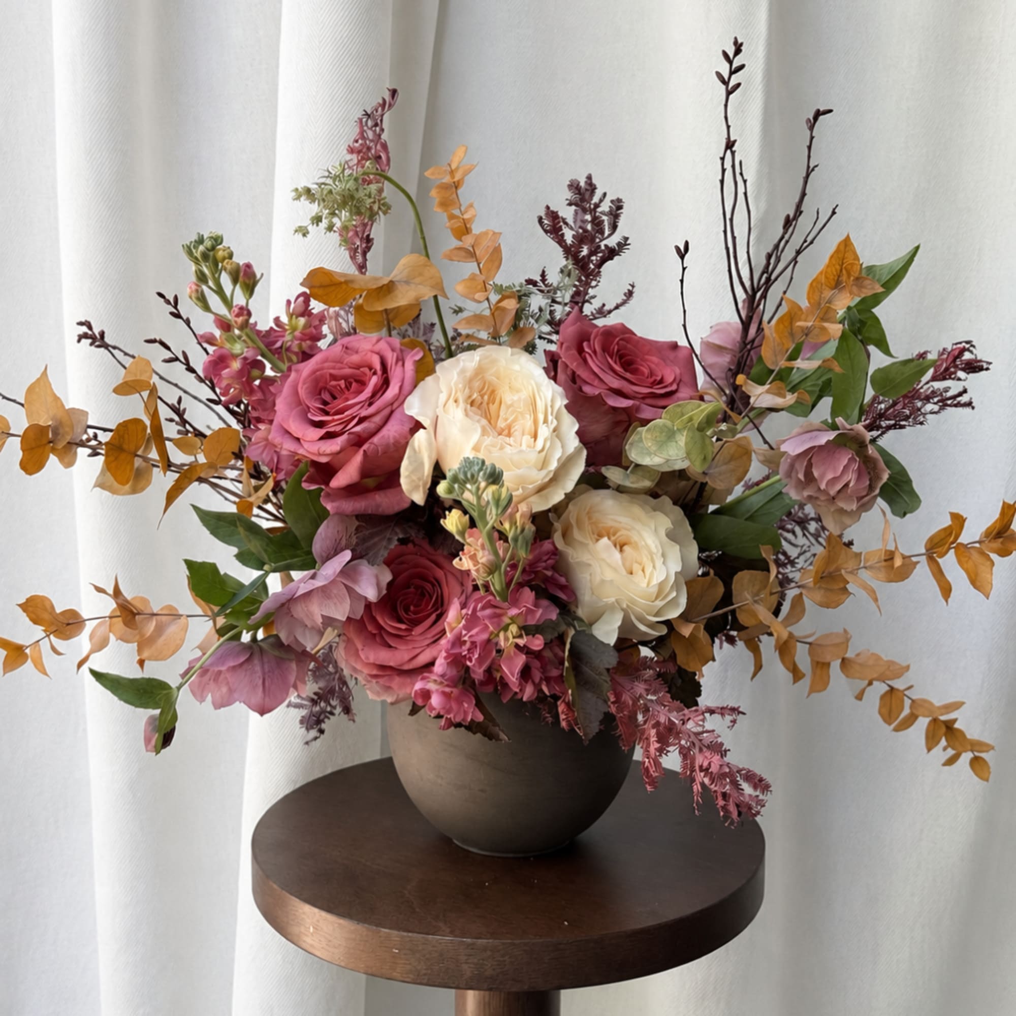 Pink and cream roses arranged in a dark vase with autumn-toned foliage
