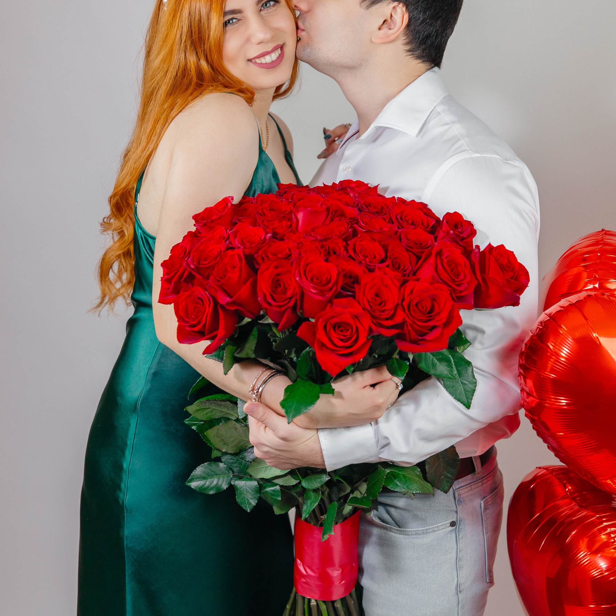 Couple holding a large bouquet of red roses with red heart balloons