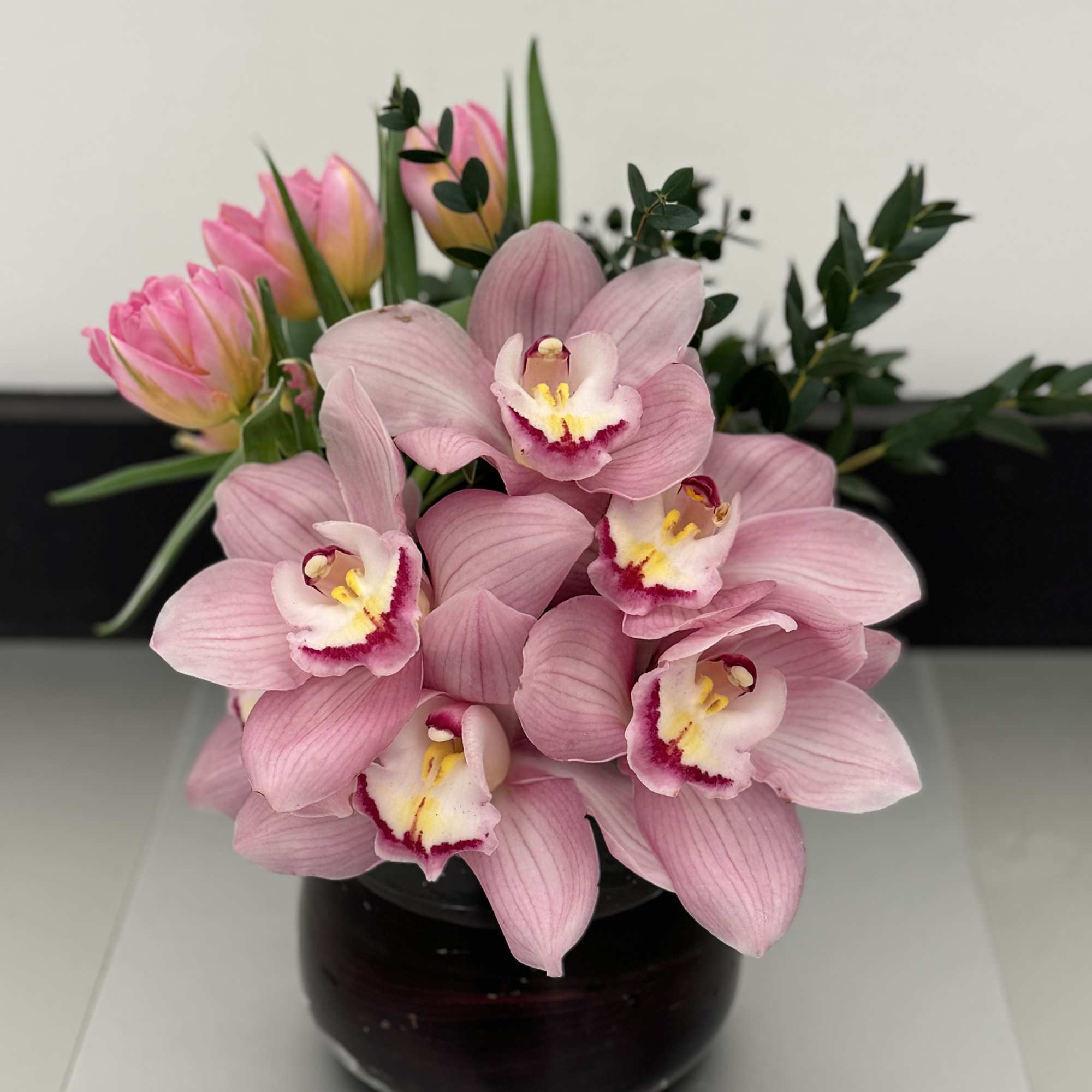 Pink orchids and tulips arranged in a dark glass vase