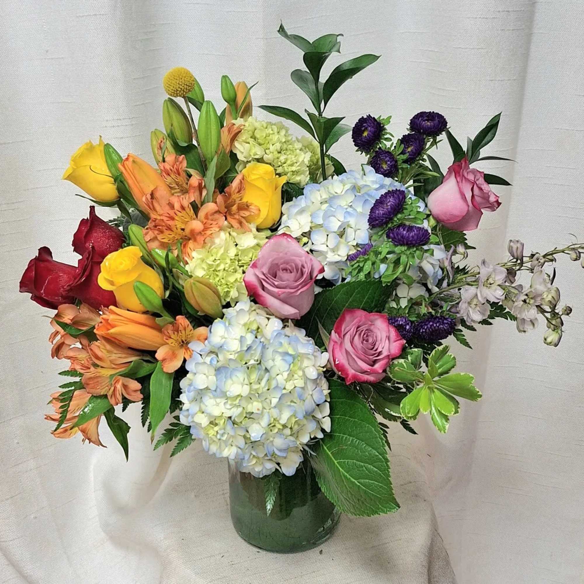 Mixed bouquet of roses, hydrangeas, lilies, and asters in a glass vase