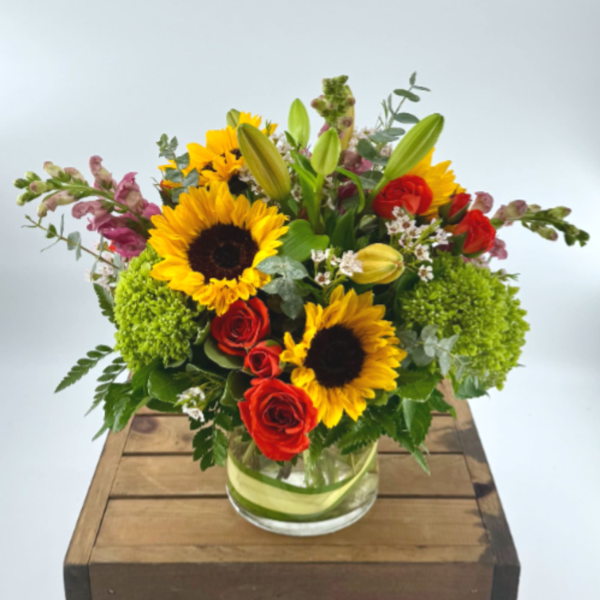 Bouquet of sunflowers, red roses, and lilies in a glass vase