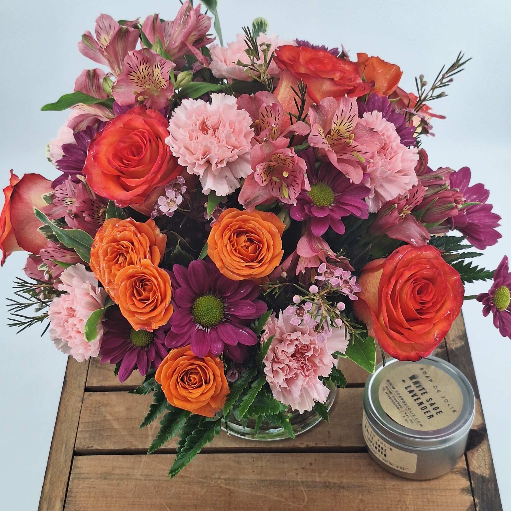 Mixed bouquet of orange roses, pink carnations, and purple daisies in a glass vase