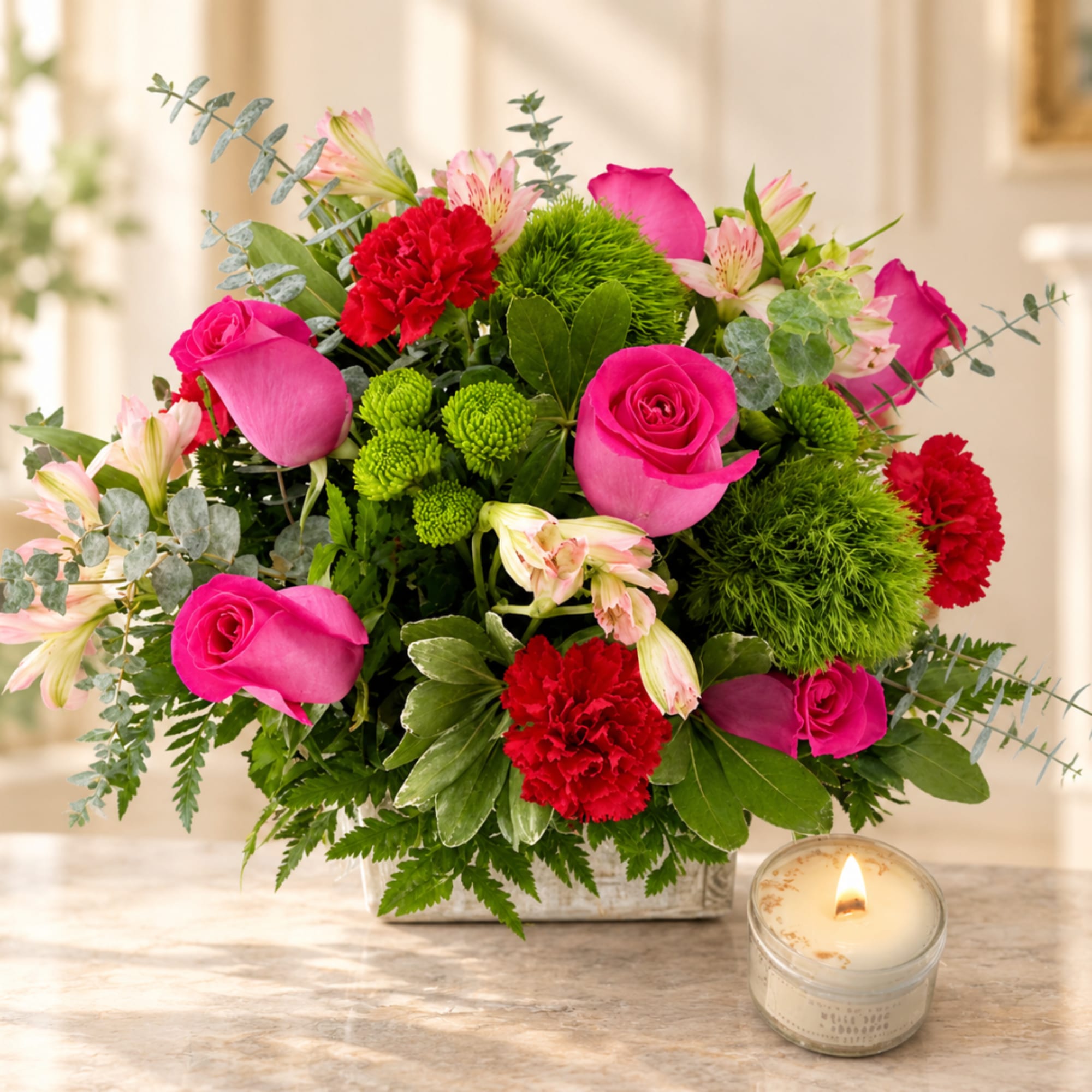 Pink roses and red carnations in a low rectangular vase with a lit candle nearby.