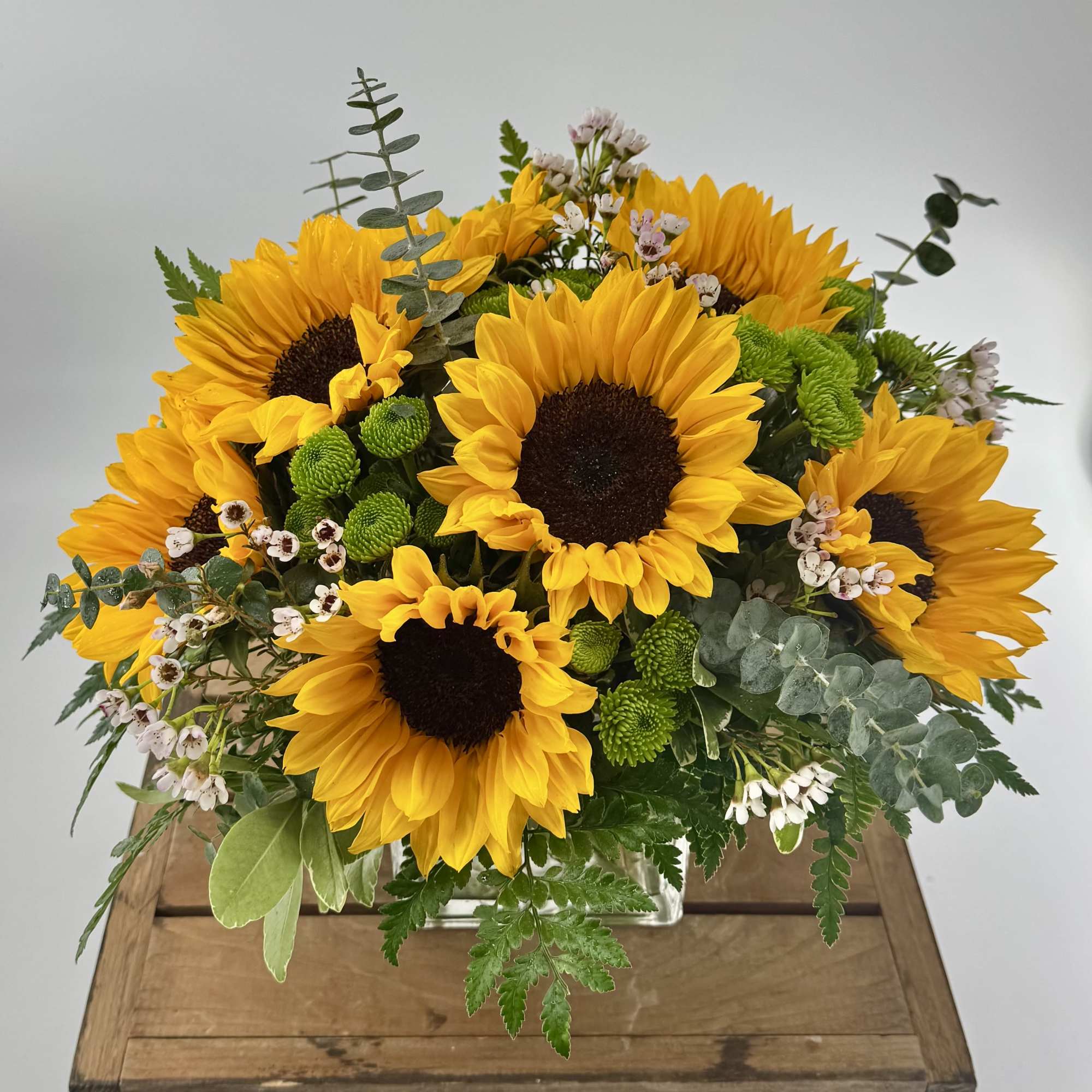 Sunflower arrangement in a clear rectangular vase with mixed greenery